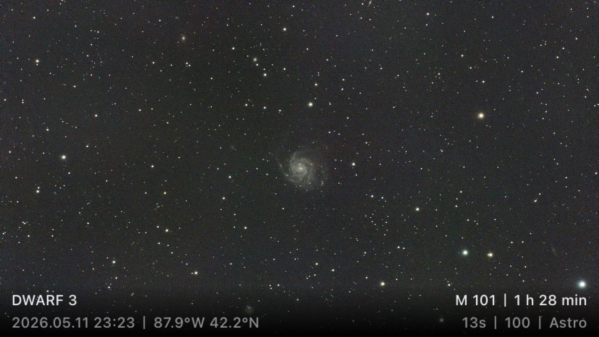 Pinwheel Galaxy (M101), a face-on spiral galaxy in Ursa Major. Its diffuse spiral arms and central core are visible within the surrounding star field, with several distant background galaxies faintly appearing throughout the image.