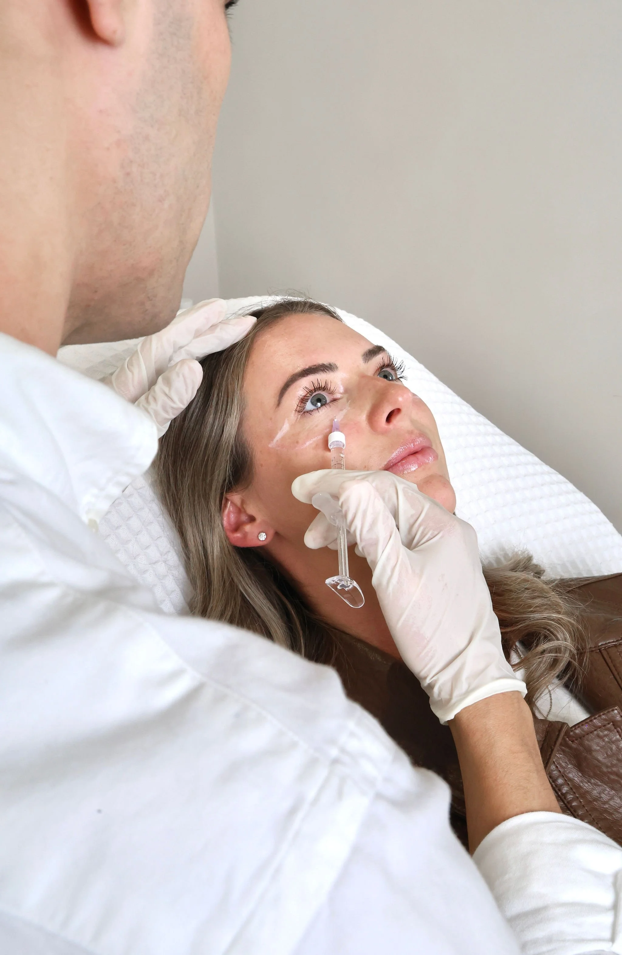 A woman receiving a cosmetic injection under her eye from a healthcare professional.