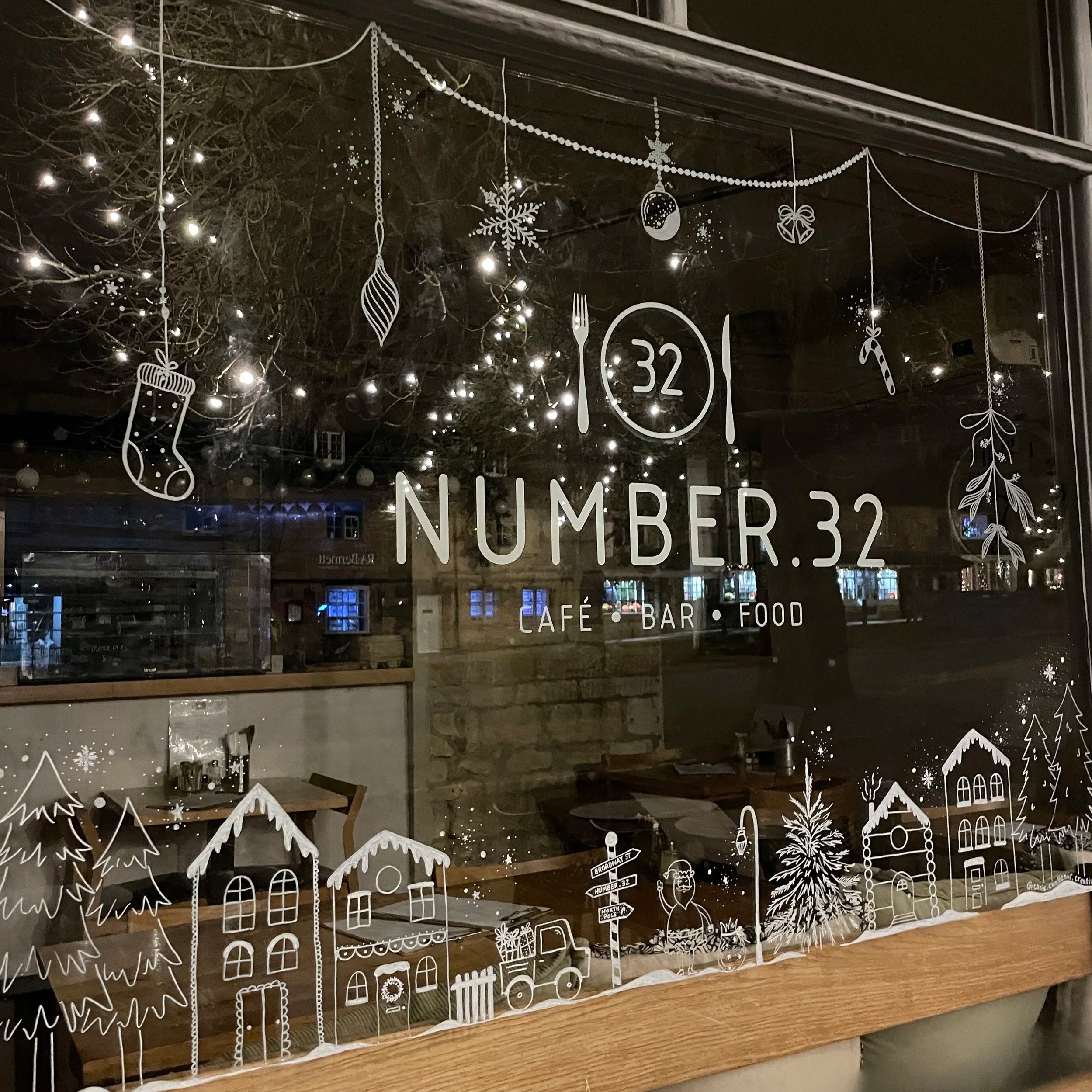 Decorative window with white snowflake, Christmas tree, and house drawings, advertising a cafe, bar, and food establishment named 'Number 32'.