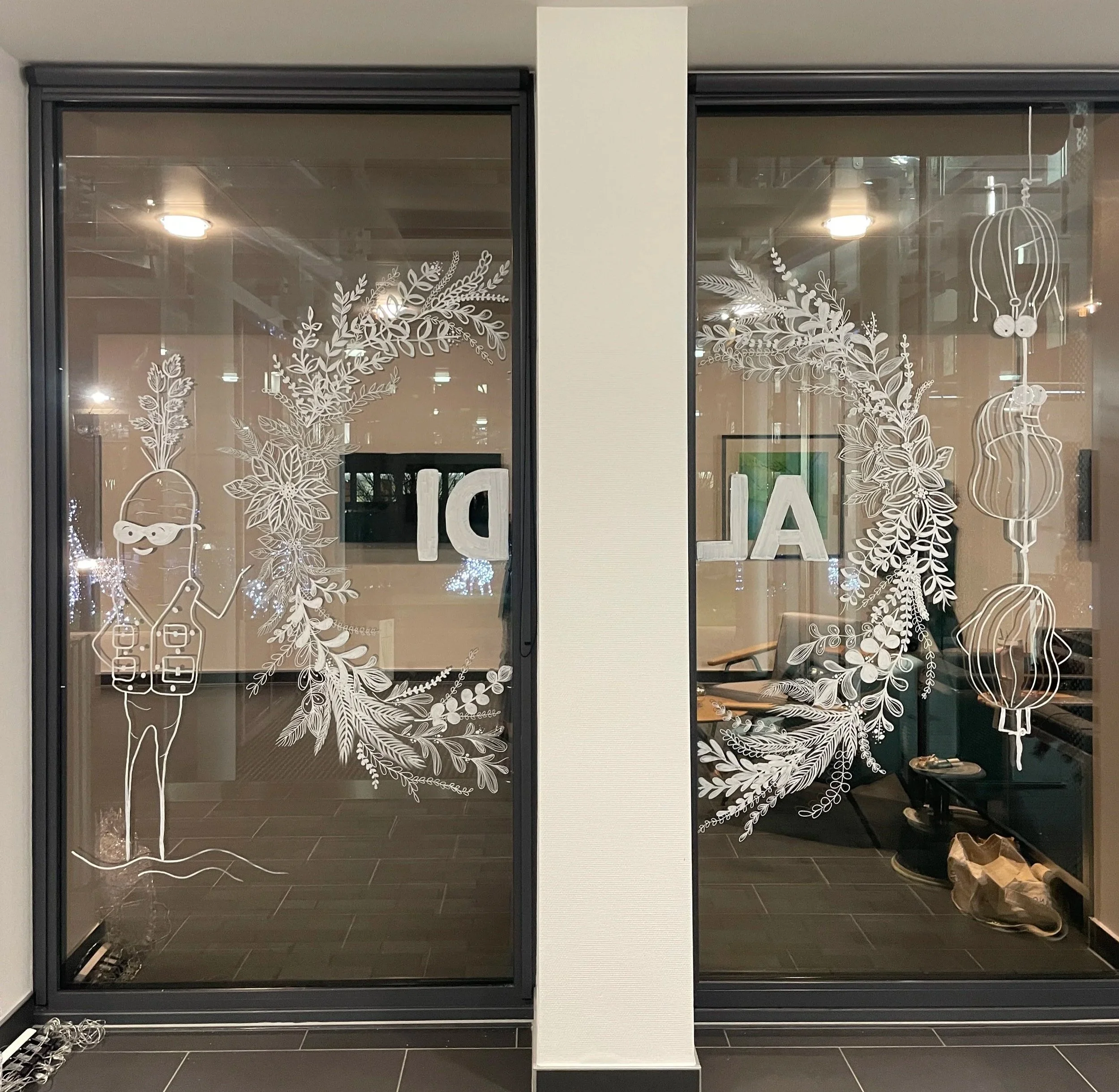 Decorative glass with drawings of a person in a hat and sunglasses, botanical wreath, the word "BAL" in reverse, and hanging lanterns and umbrellas.