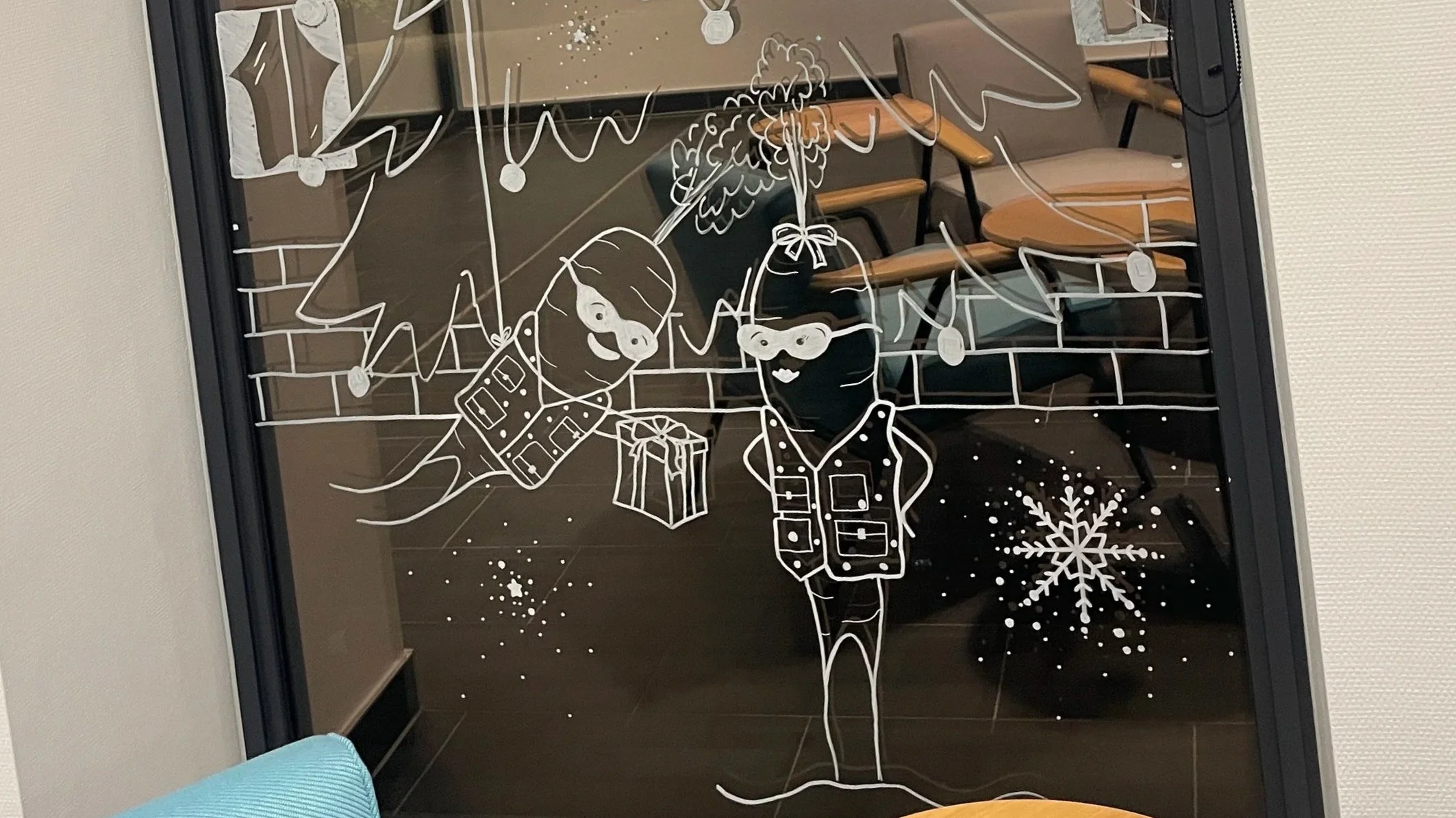 Decorative window cling with a white line drawing of two children in winter clothing exchanging gifts, with snowflakes and hanging ornaments on glass