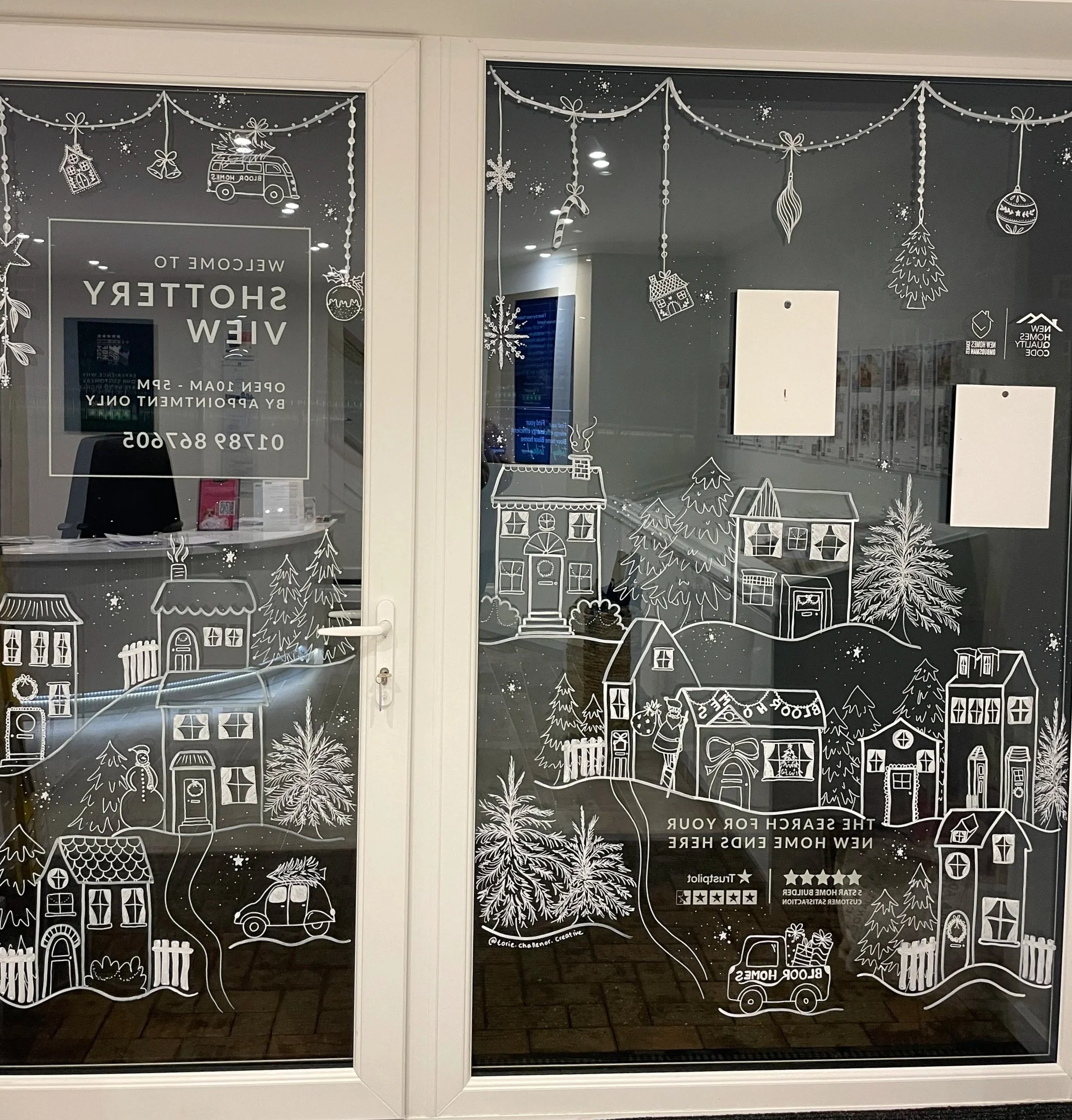Holiday-themed window decal featuring houses, trees, snowflakes, ornaments, and a delivery truck with the message 'The search for your new home ends here'.