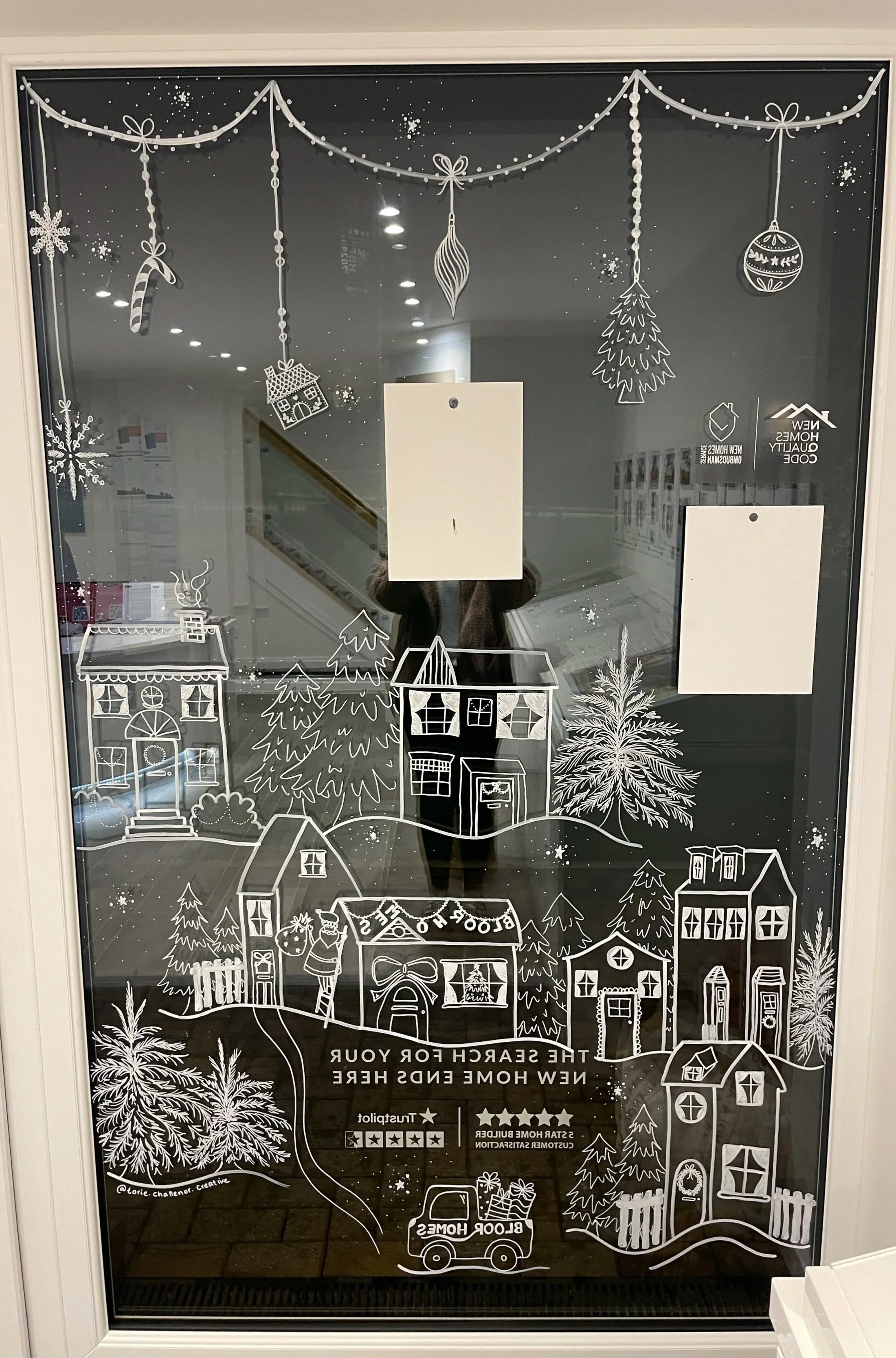 Decorative holiday window decals of snowflakes, ornaments, trees, houses, and a person with a gift, conveying a festive winter scene.