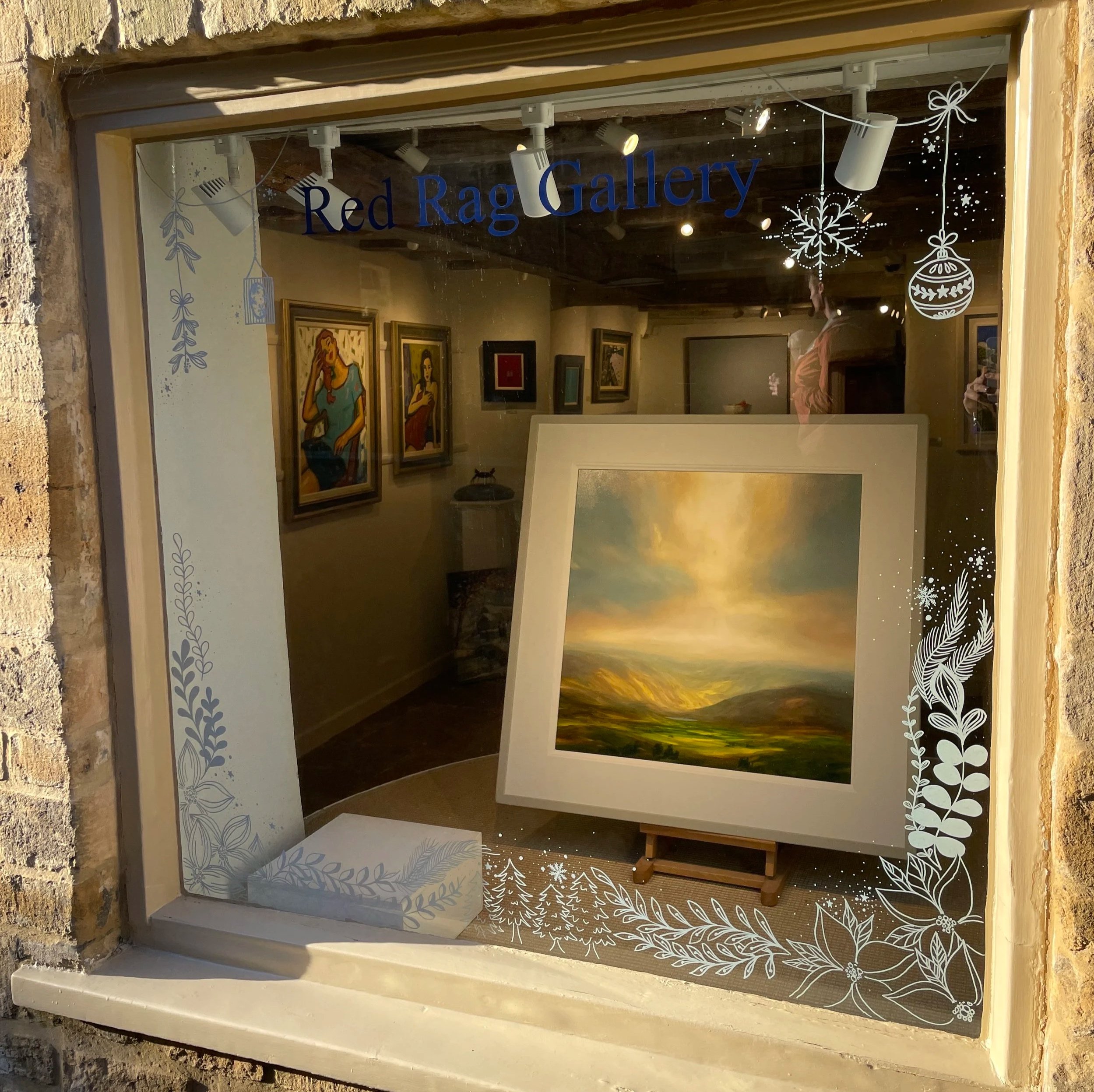 Gallery window with paintings inside, labeled "Red Rag Gallery," decorated with holiday-themed snowflakes and foliage graphics.