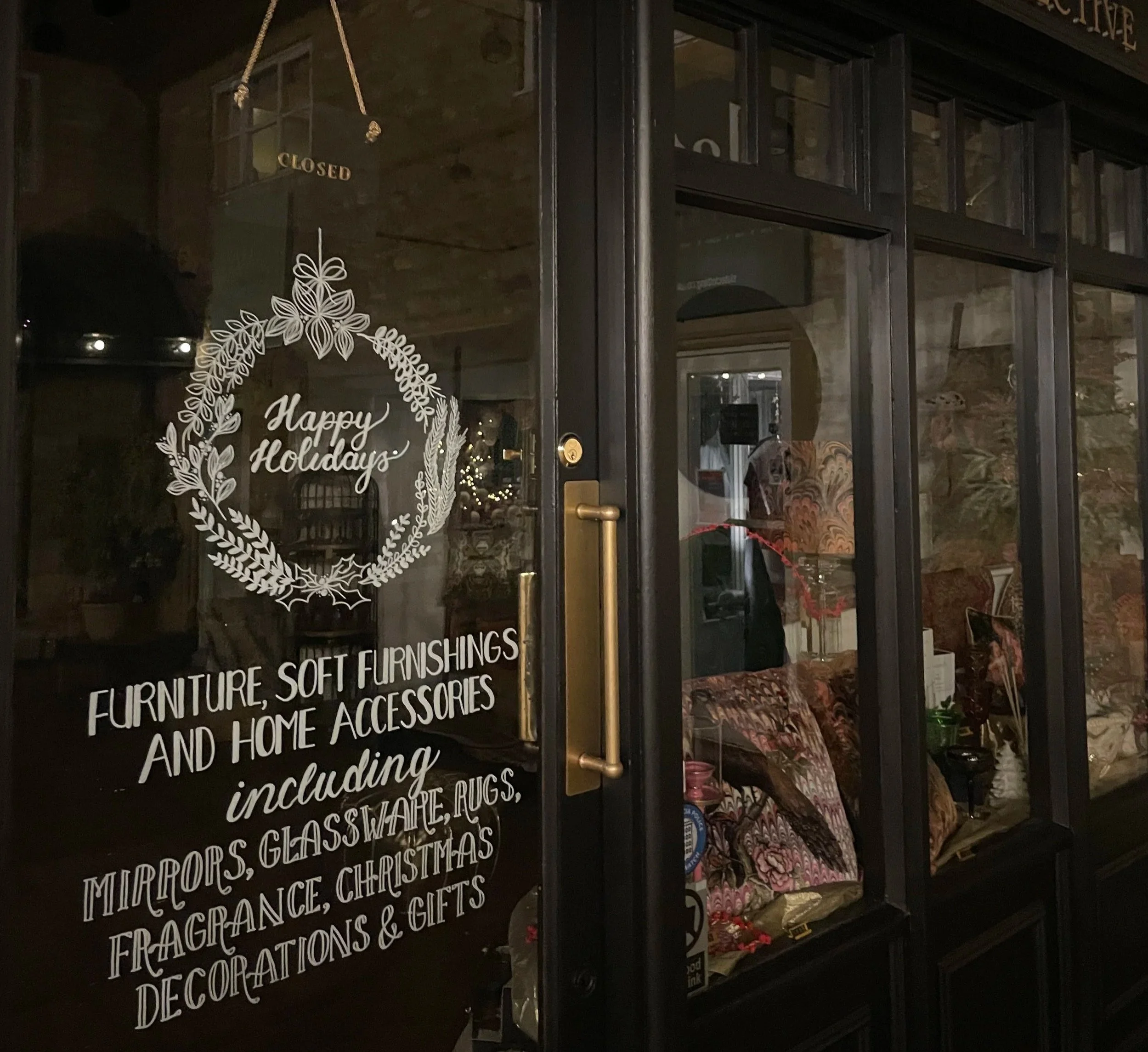 Decorative glass door with a holiday message and signage for a furniture and home accessories store. The sign says, 'Happy Holidays' and lists items like mirrors, glaze, rugs, fragrance, Christmas decorations, and gifts.