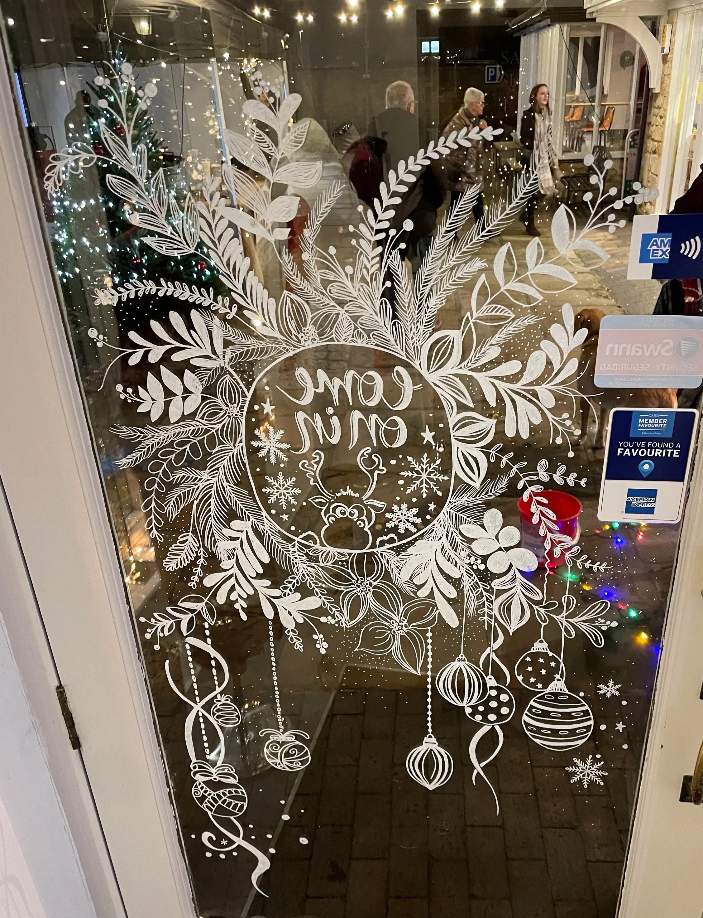 Decorative holiday door window with white illustrations of leaves, snowflakes, ornaments, and a Central circle with the words 'Joy to the World' inside.