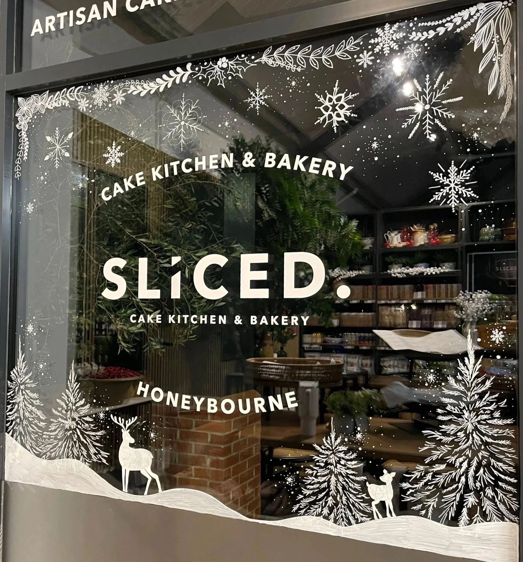 Decorative window featuring window art of snowflakes, pine trees, and reindeer, with text that reads 'SICEO. CAKE KITCHEN & BAKERY' and 'HONEYBOURNE'