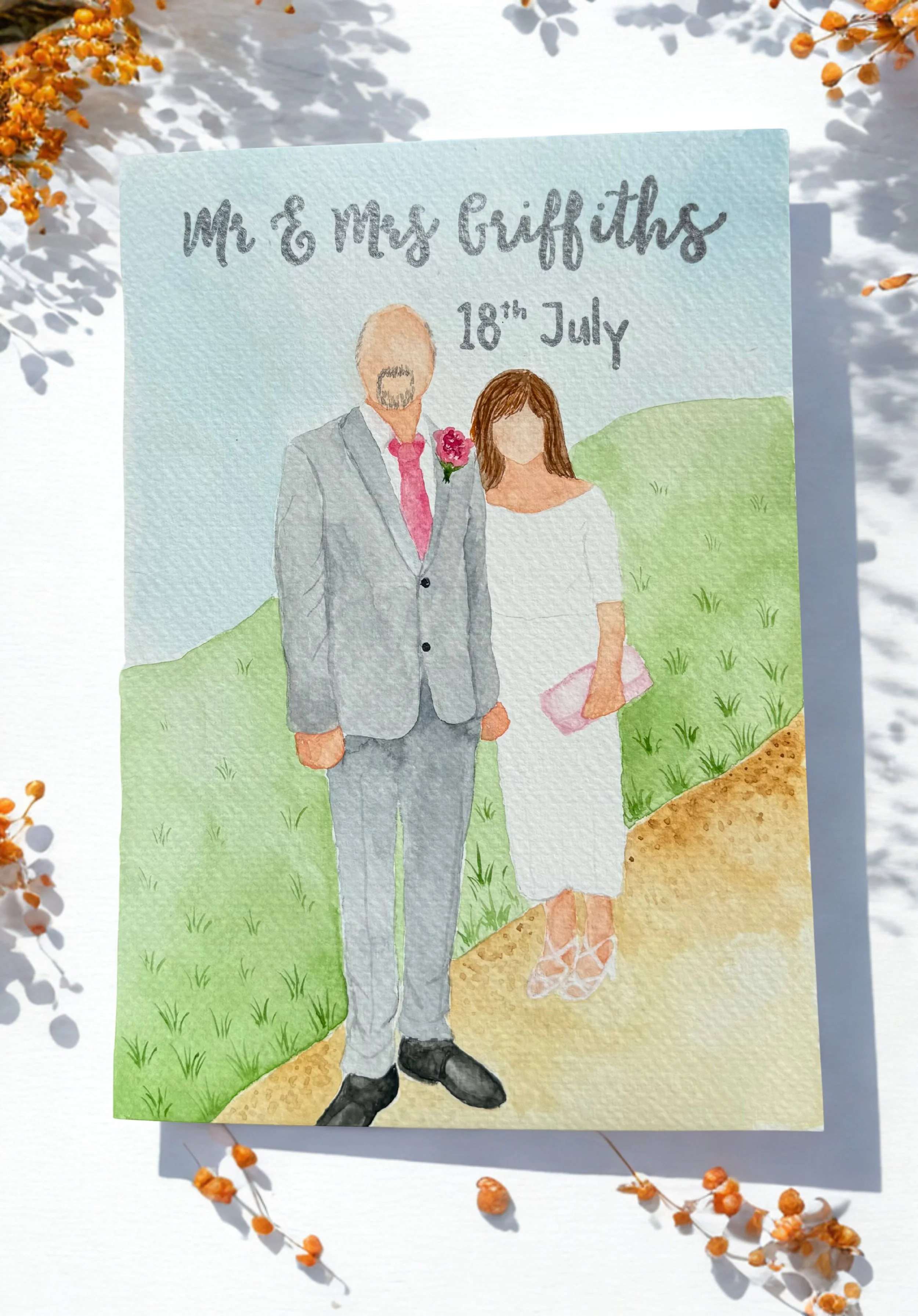 Watercolor illustration of a wedding invitation featuring a couple dressed in formal clothes, the man in a gray suit with a pink tie and flower boutonniere, and the woman in a white dress with pink shoes, standing outdoors on a grassy path with sunlight and orange flowers around.