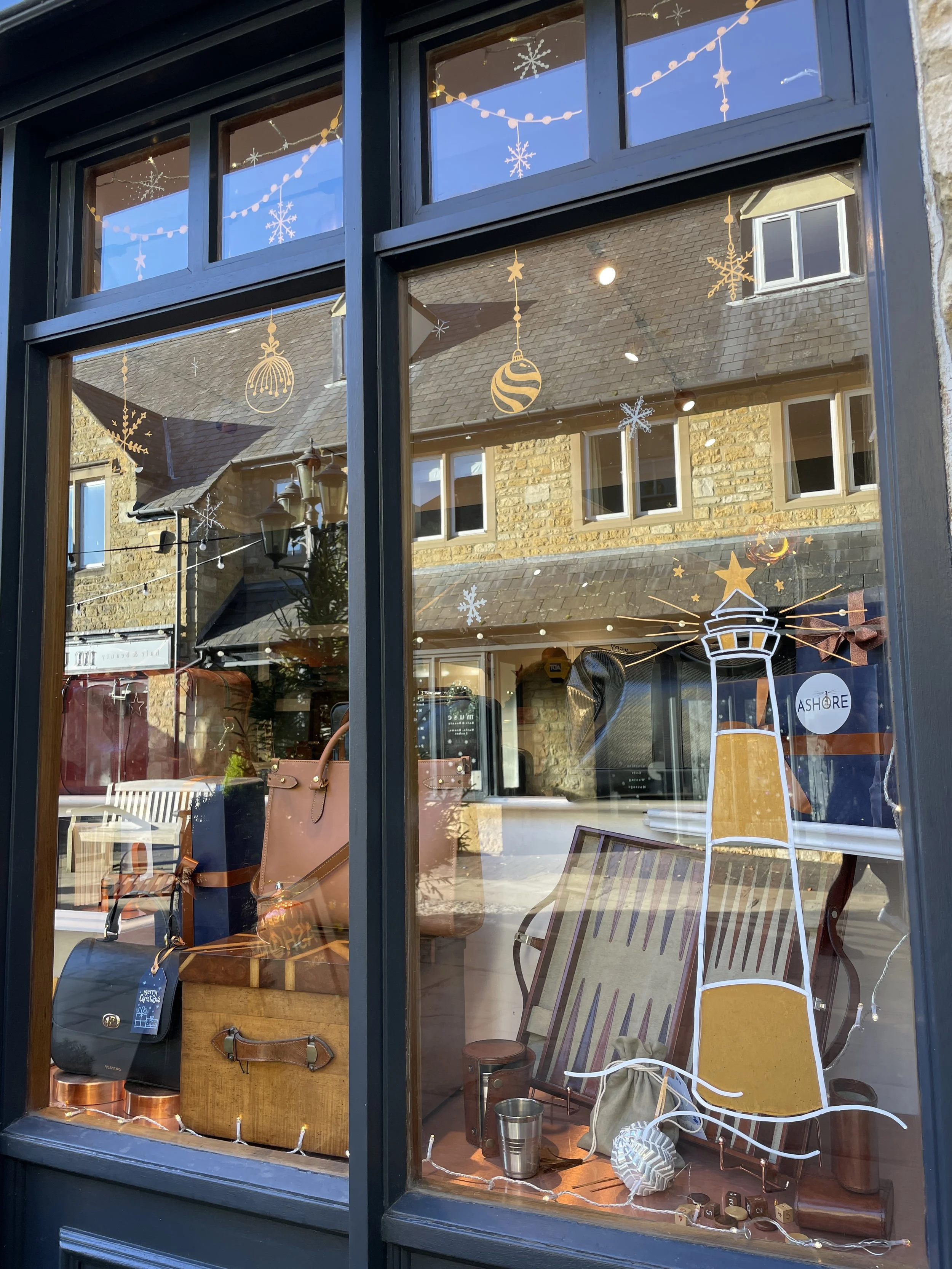 Shop window decorated with Christmas ornaments and snowflakes, with various items such as bags, suitcases, and a small lantern inside.