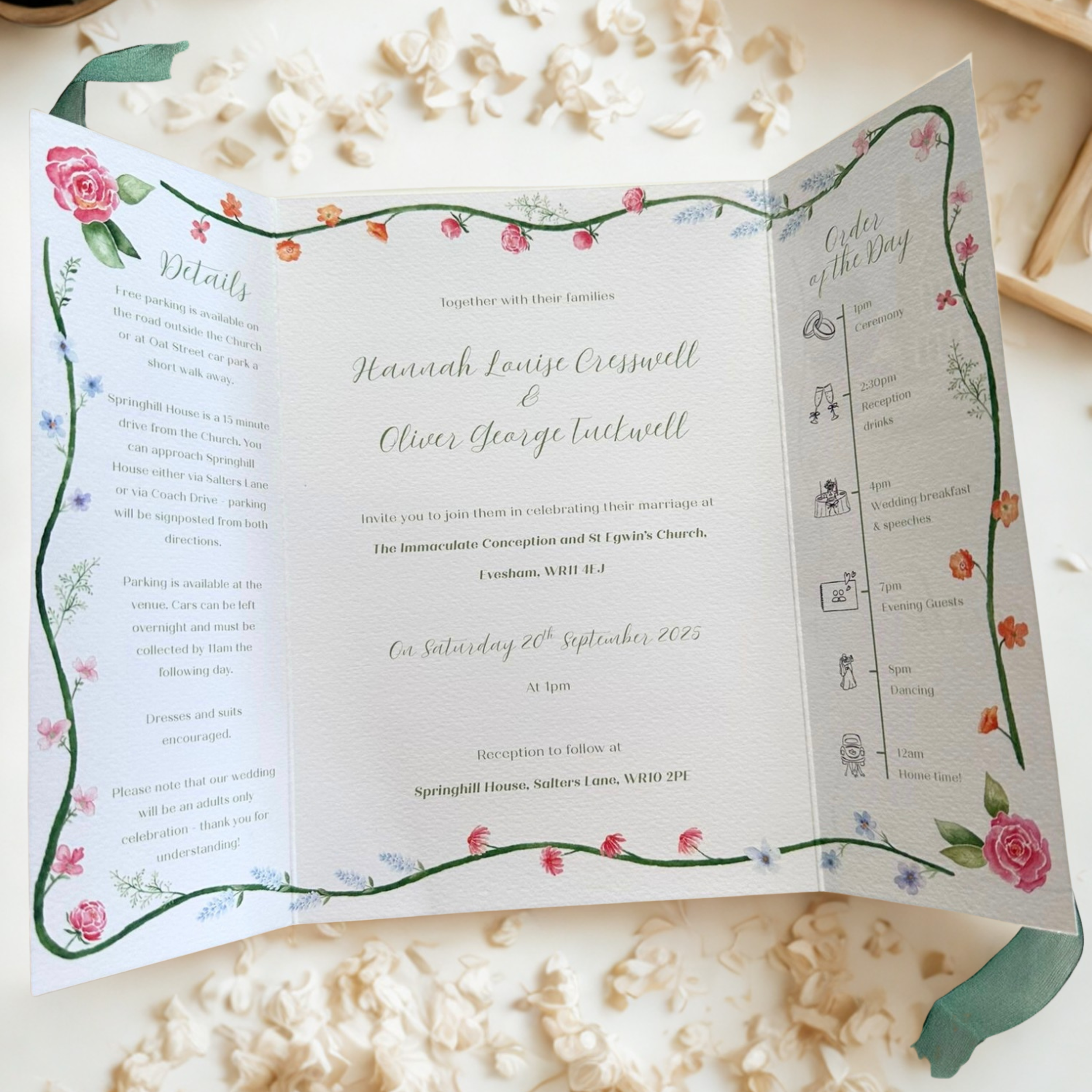 A wedding invitation card with floral decorations and schedule details placed on a surface with scattered flower petals.