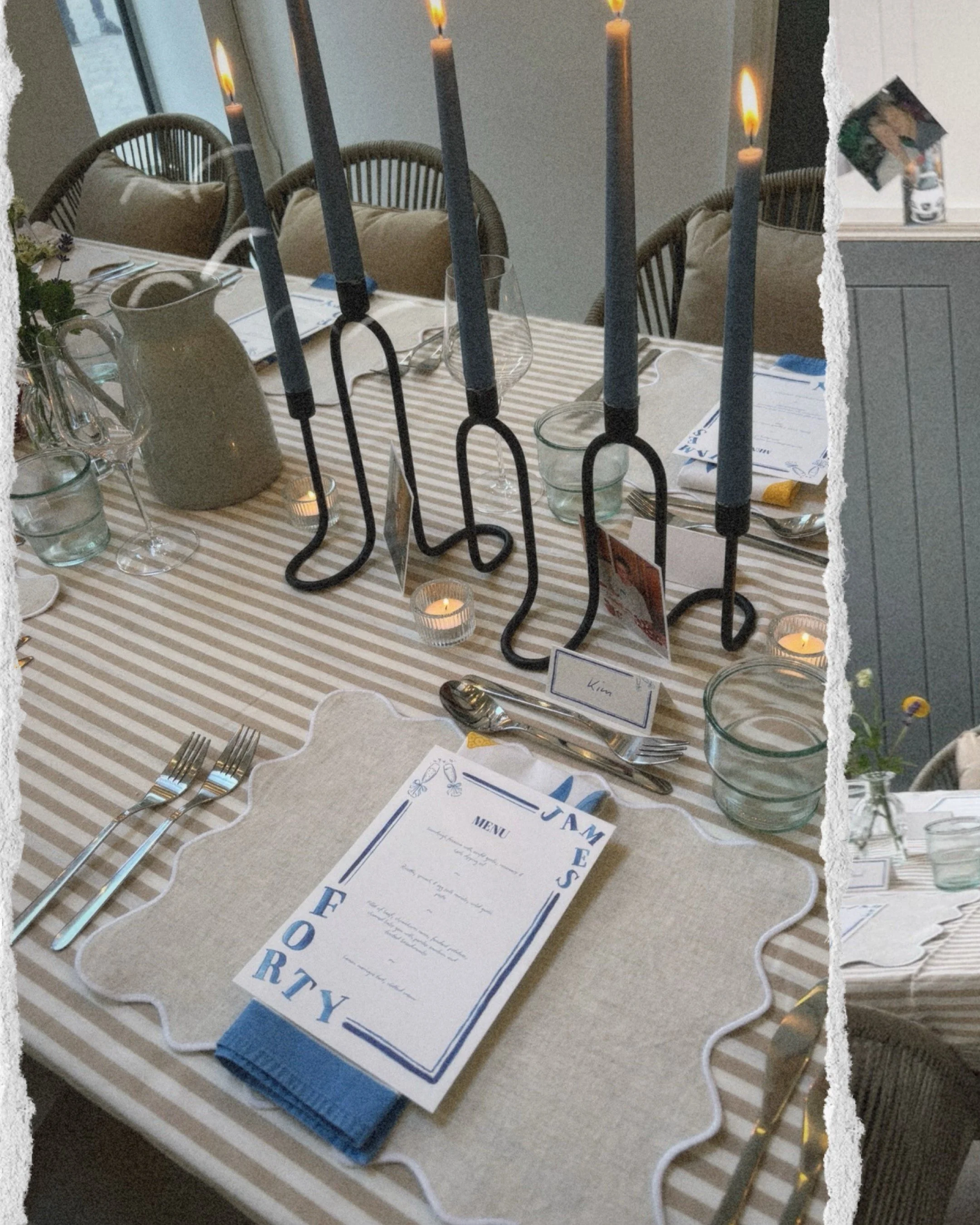 Elegant dining table set with striped tablecloth, candles, place settings including forks, knives, glasses, menus, and decorative black candle holders, in a cozy, well-lit room.