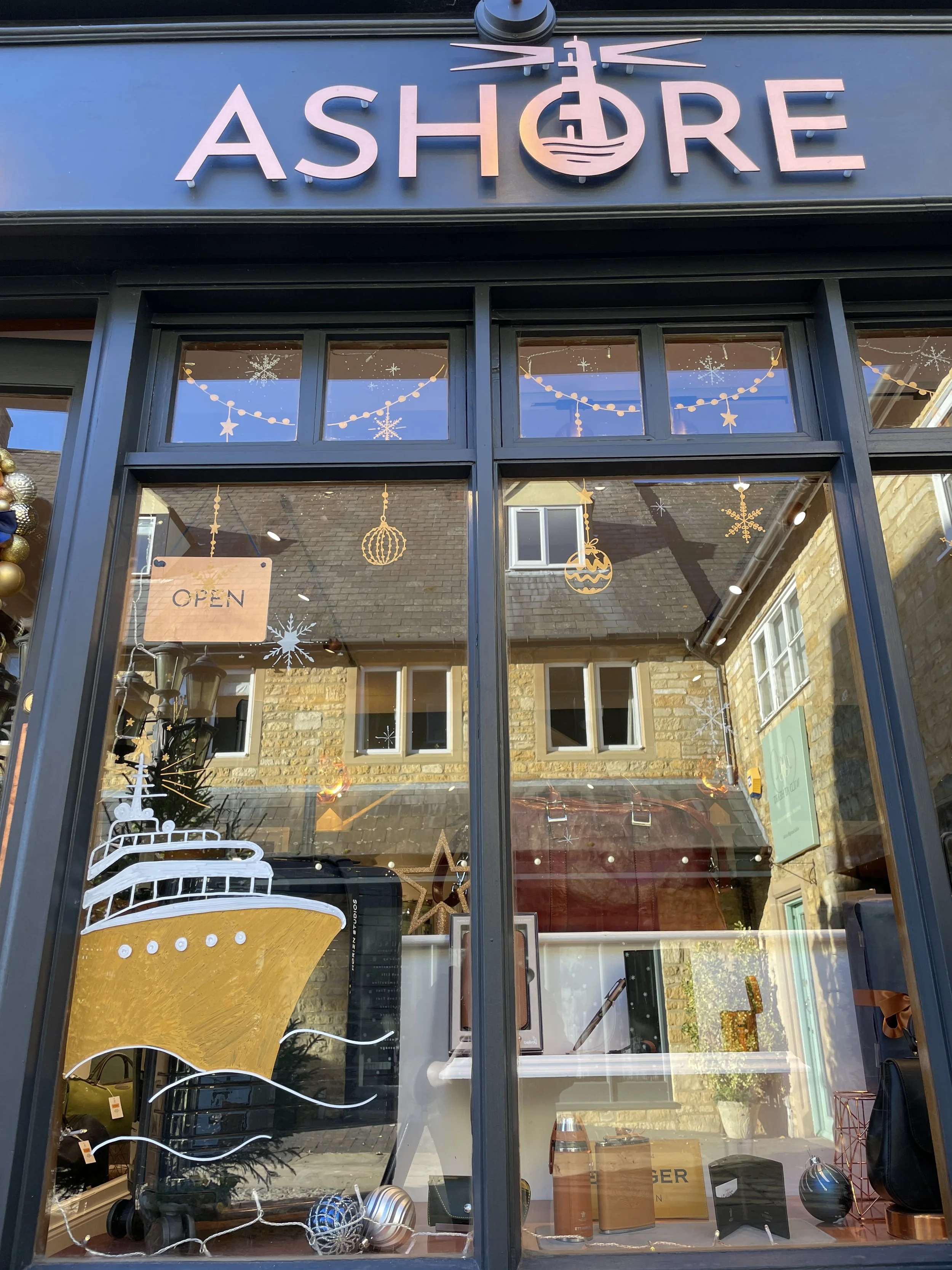 Storefront window decorated with Christmas ornaments and snowflake decals, with the name 'Ashore' on the sign above the door.