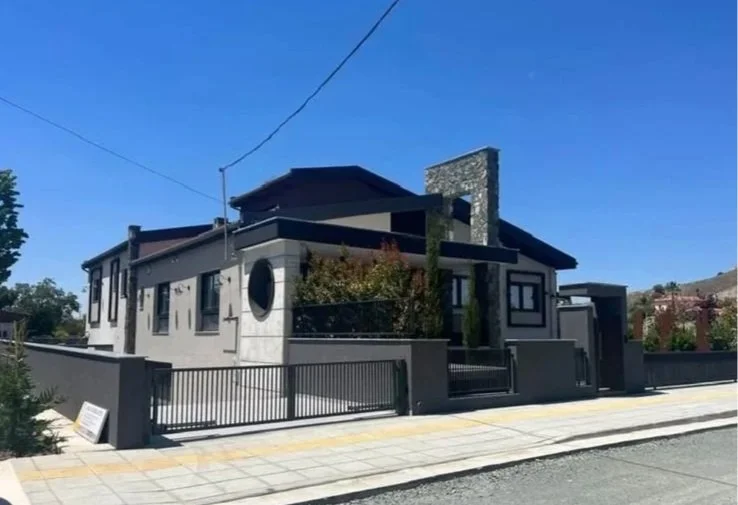 Modern house with gray and black exterior, surrounded by a black metal fence, on a sunny day.