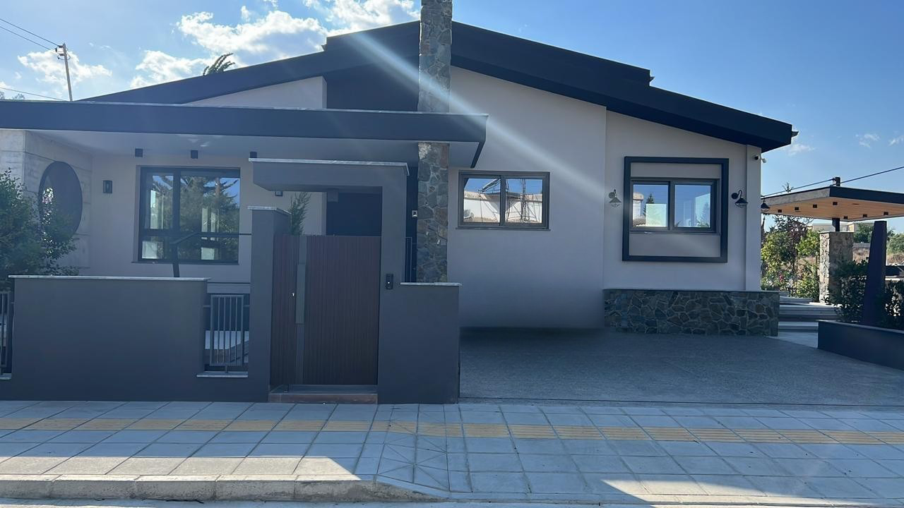 Modern house with white walls, black window frames, and stone accents, with a gate and sidewalk in front.