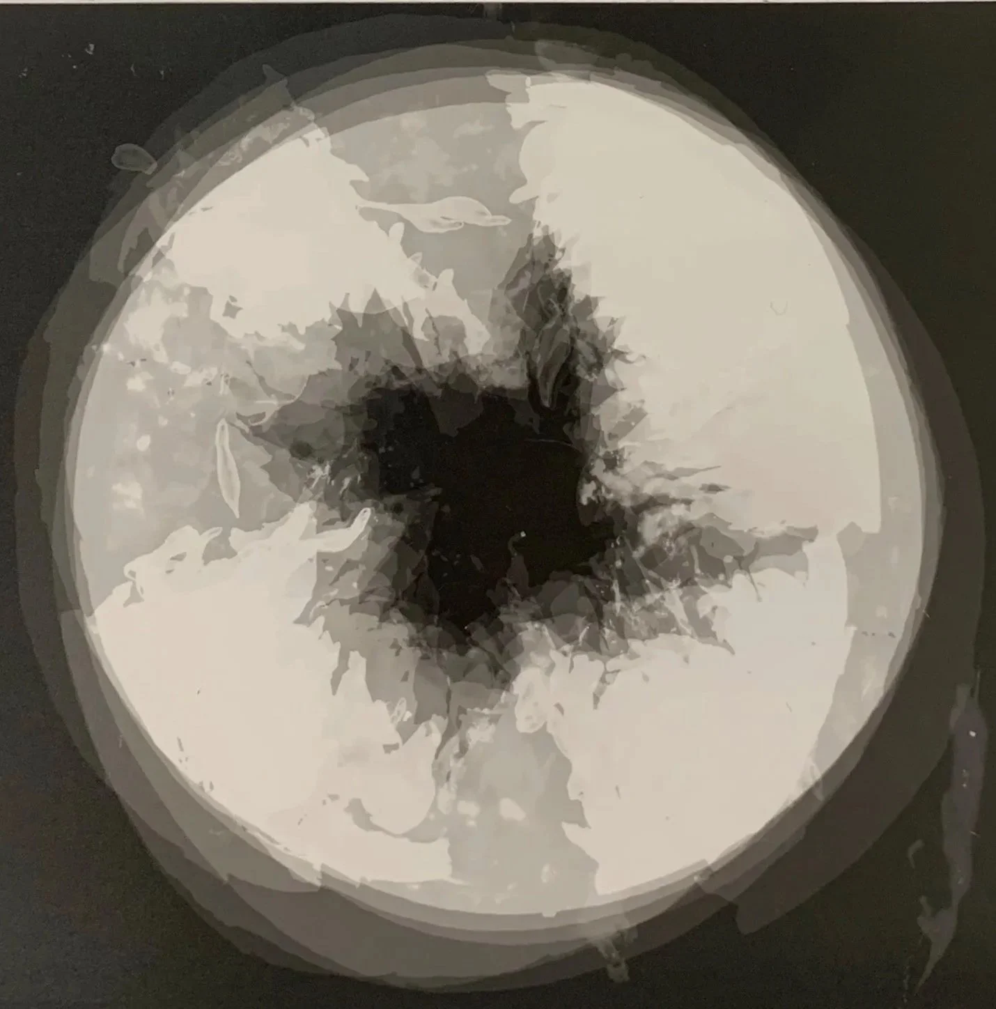 Black and white abstract image resembling a central dark hole with splattered edges on a light background, circular shape, with irregular shading and streaks.