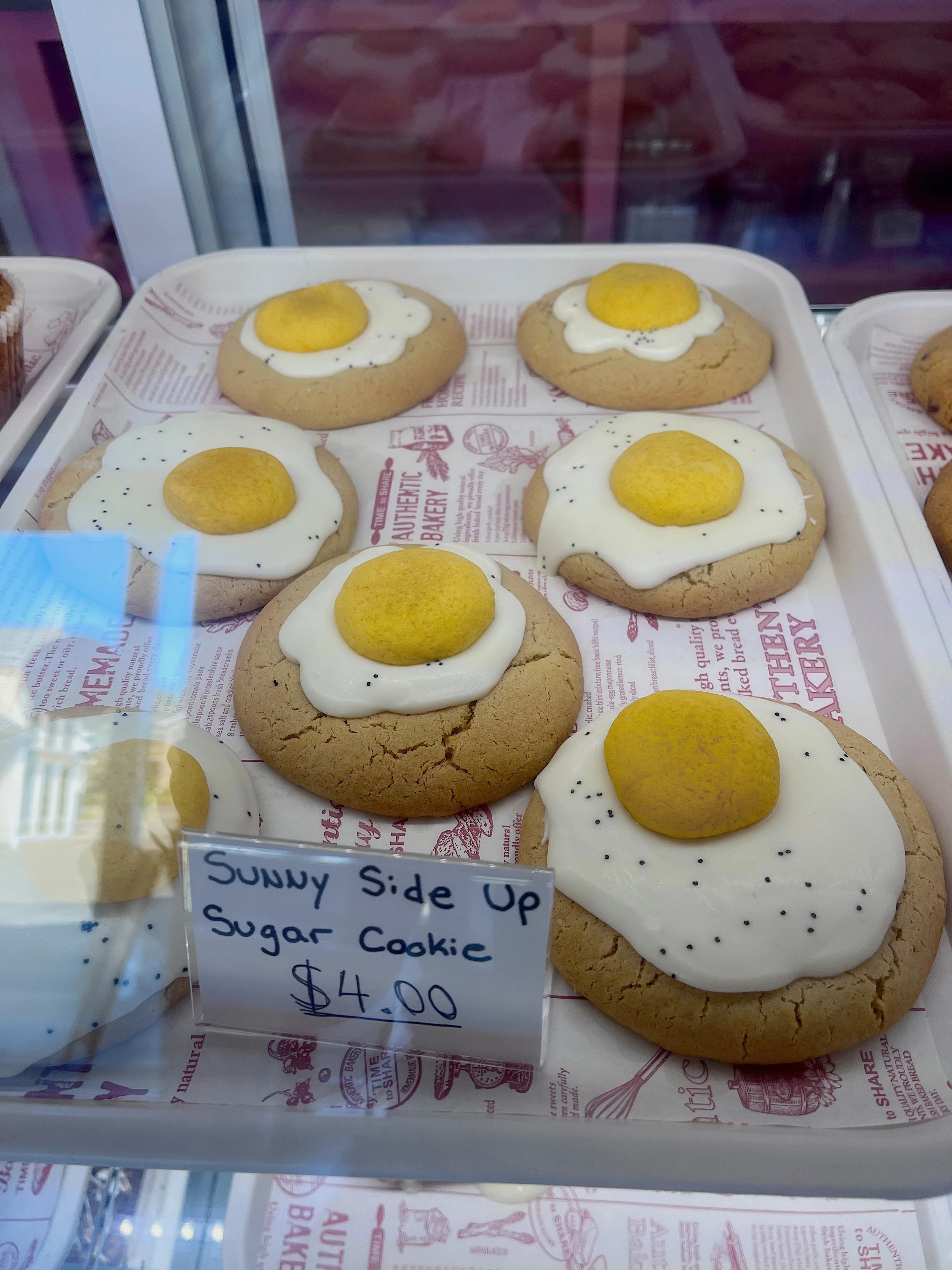 Cookies with white icing, a yellow round candy on top, and black sprinkles, labeled as Sunny Side Up Sugar Cookies priced at $4.00.