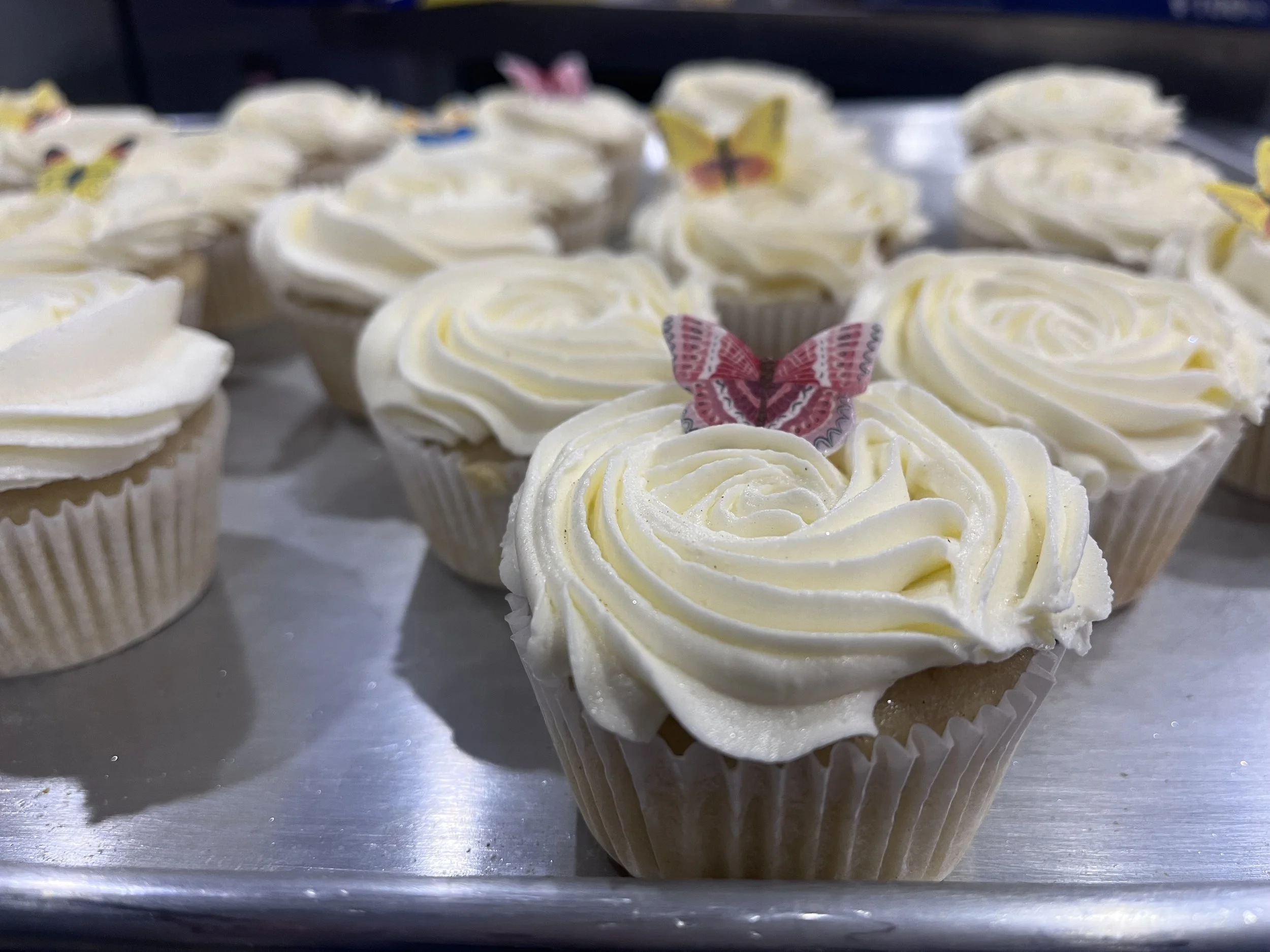 Close-up of cupcakes with white frosting and pink butterfly decoration.