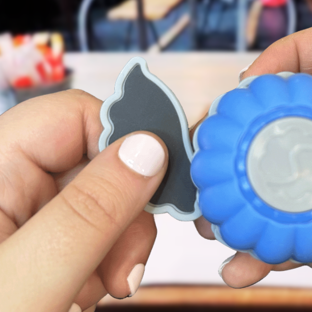 Close-up of two hands holding a blue and gray bubble-shaped object and a coin-shaped rubber toy.