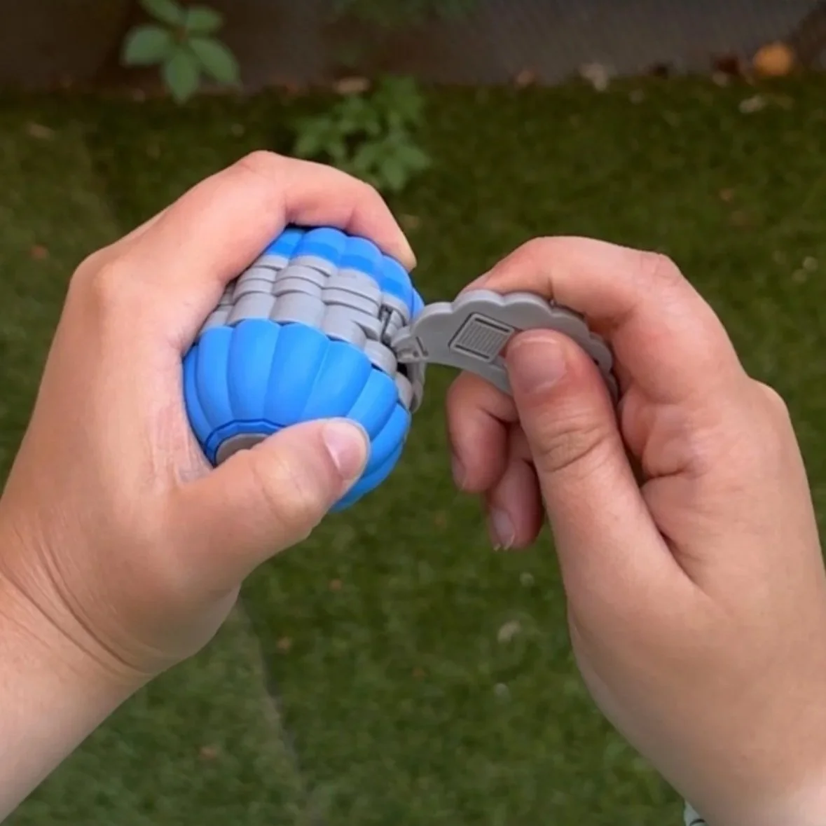 Close-up of a person holding a small, blue and gray, expandable, portable object, with one hand taking a wing out and the other gripping the SIDEKICK™️.