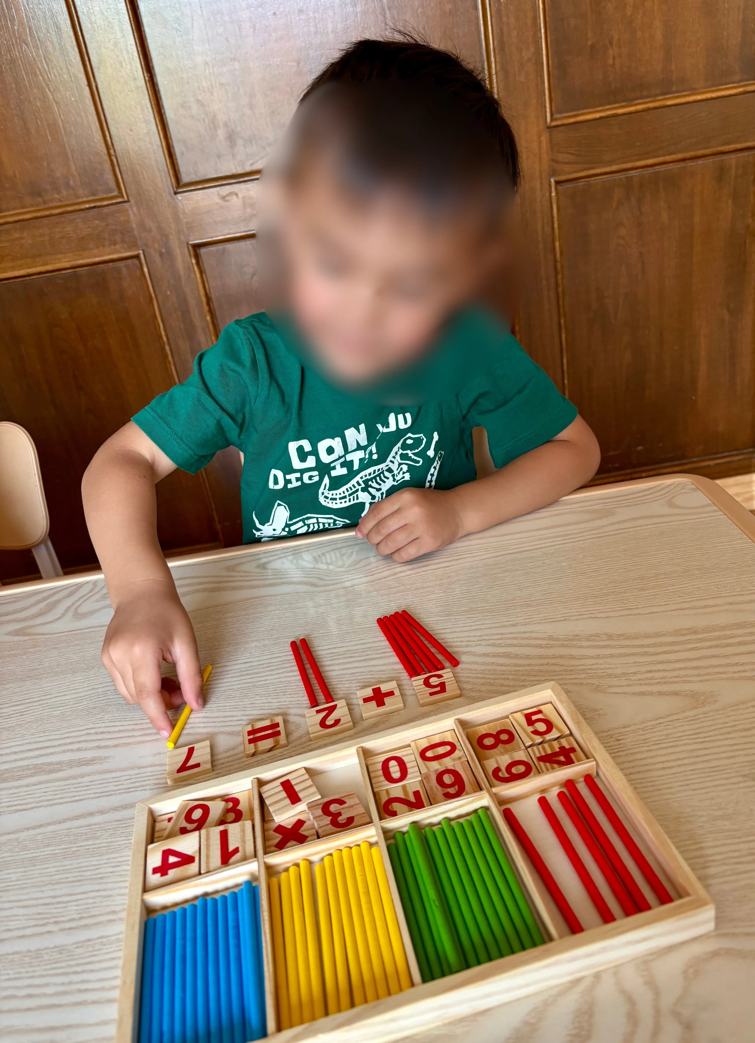 Child playing with colorful educational math toys, sorting number and calculation blocks at a wooden table with a wooden wall background.