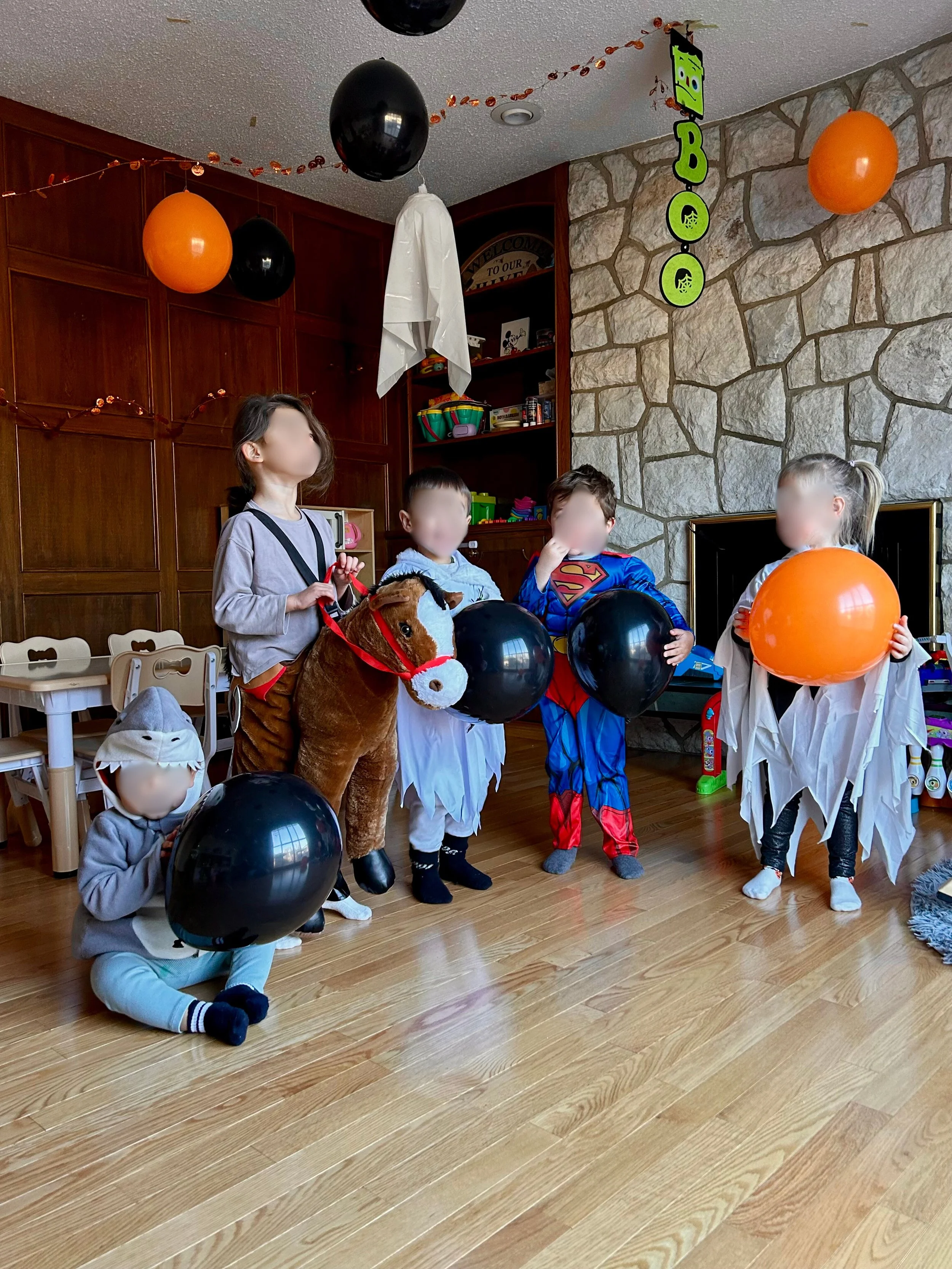 Children in costumes holding balloons at a Halloween party in a decorated living room.