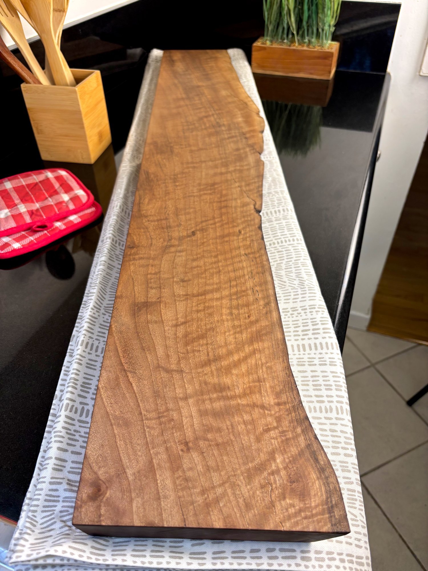 Walnut charcuterie board, set on top of decorative table runner and black countertop.