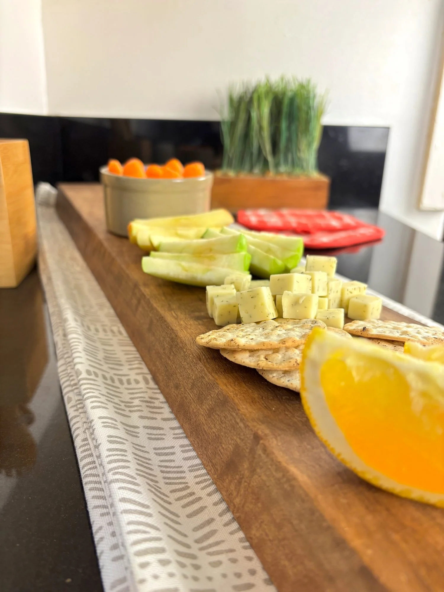 Walnut charcuterie board, set on top of decorative table runner and black countertop.