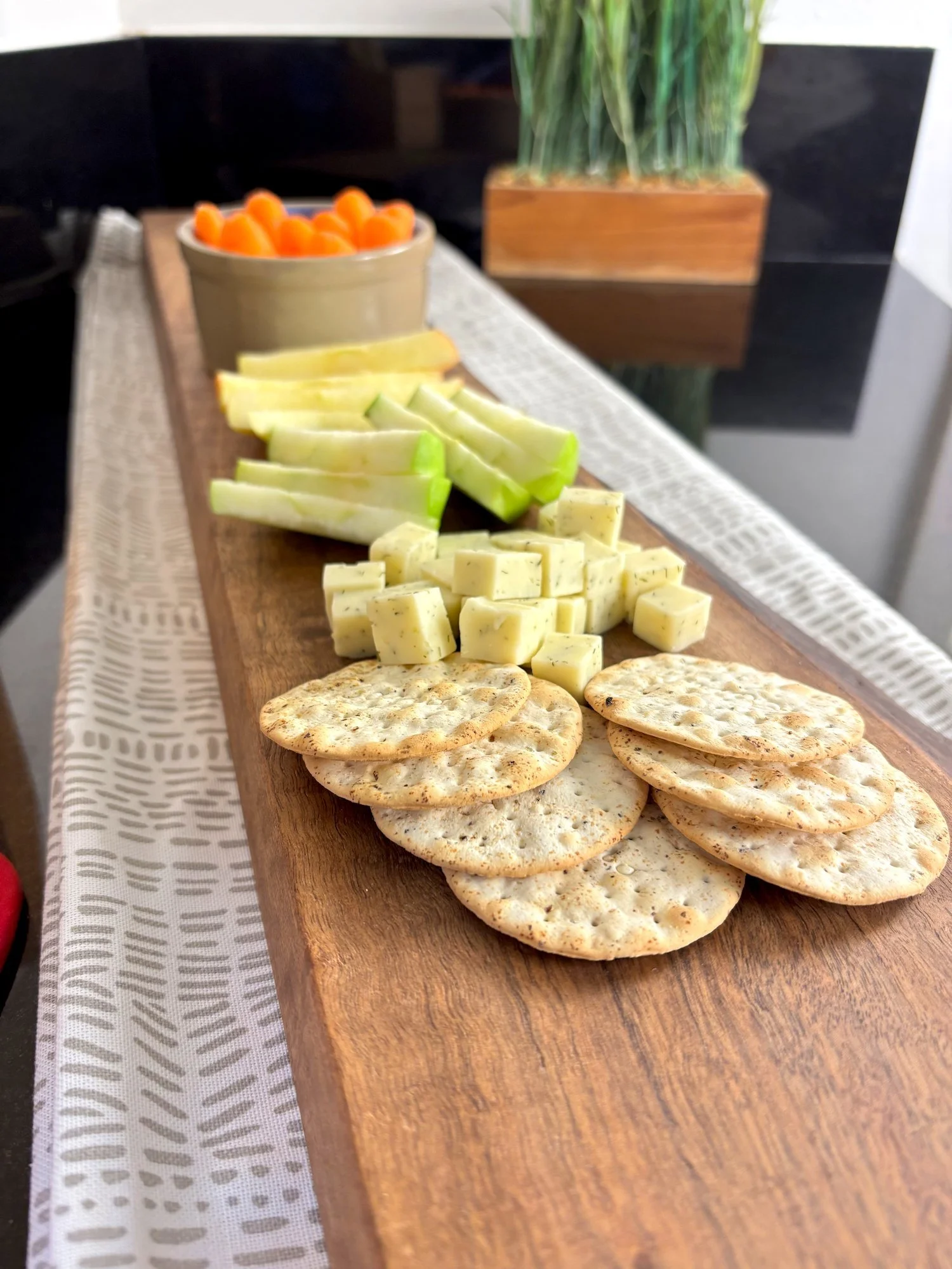 Walnut charcuterie board, set on top of decorative table runner and black countertop.