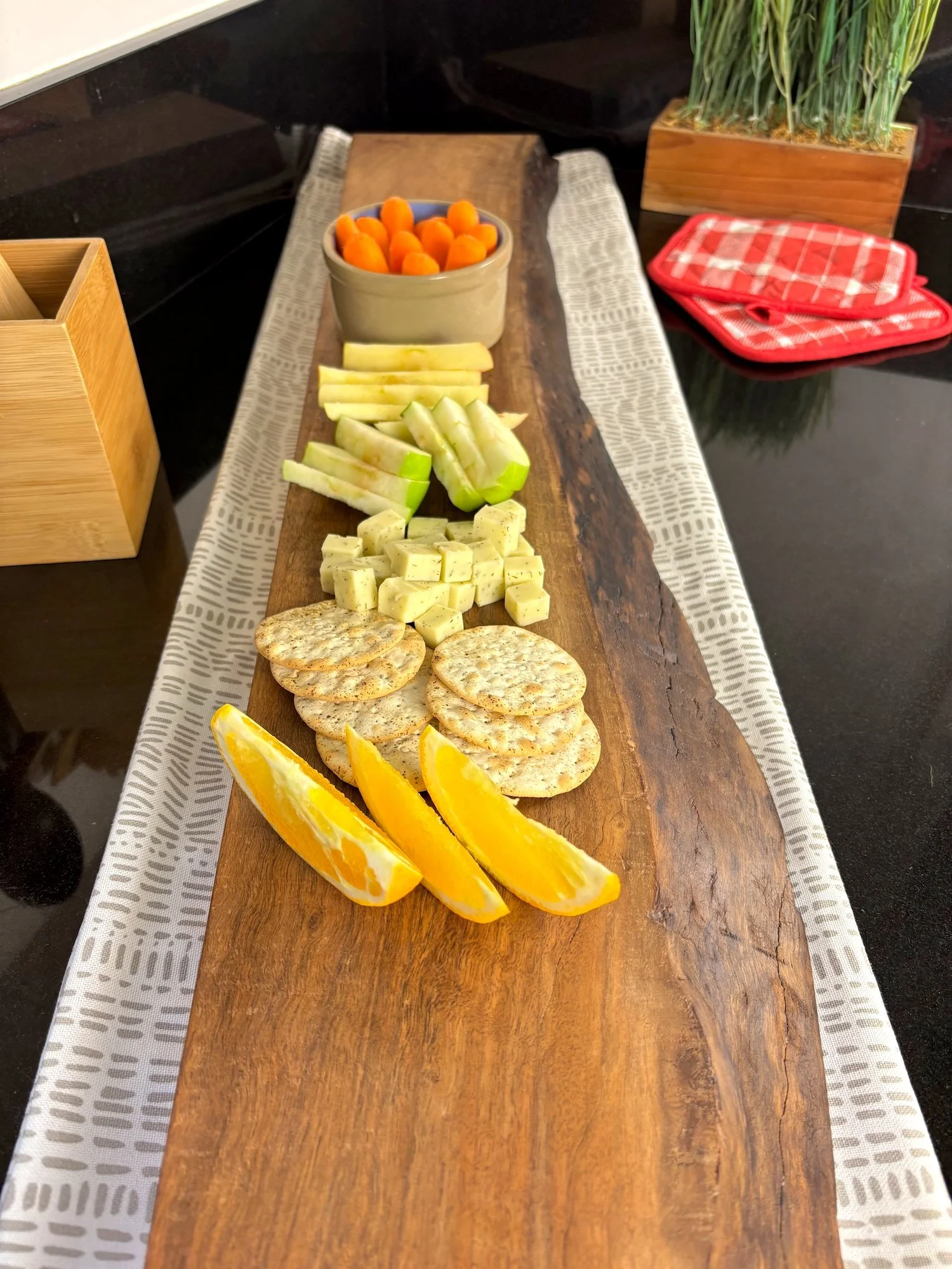 Walnut charcuterie board, set on top of decorative table runner and black countertop.
