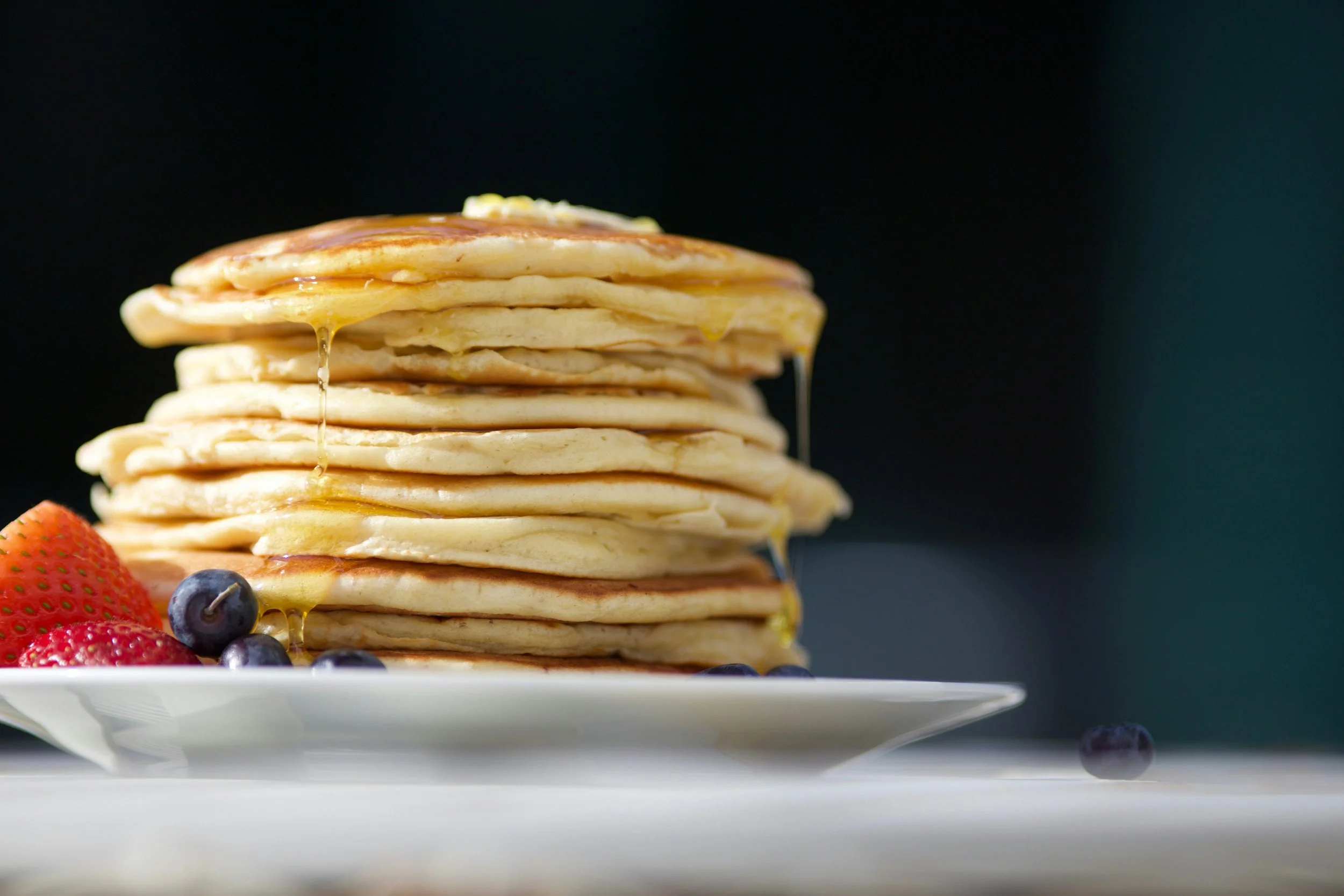 Stack of pancakes with syrup and fresh berries on a white plate.