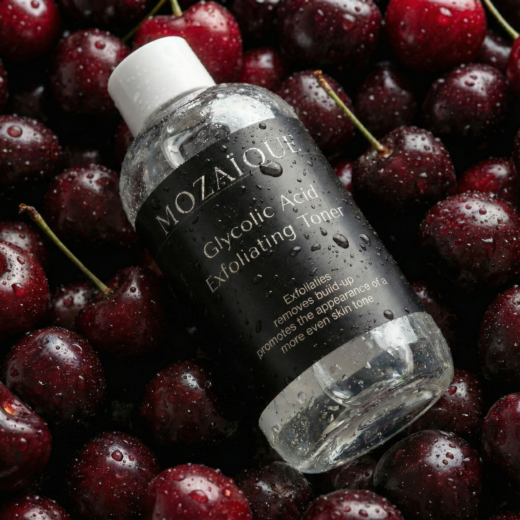 A bottle of MOIZIQUE Glycolic Acid Exfoliating Toner lying on wet cherries.