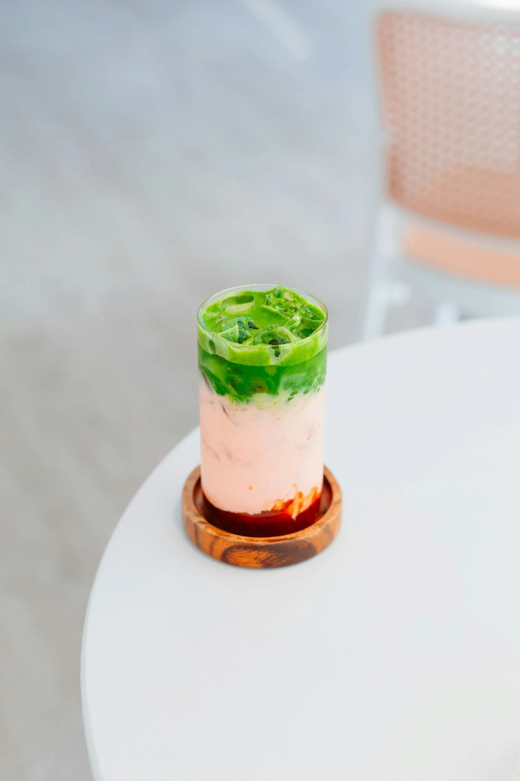 A glass of matcha latte with milk and green tea sitting on a wooden table.