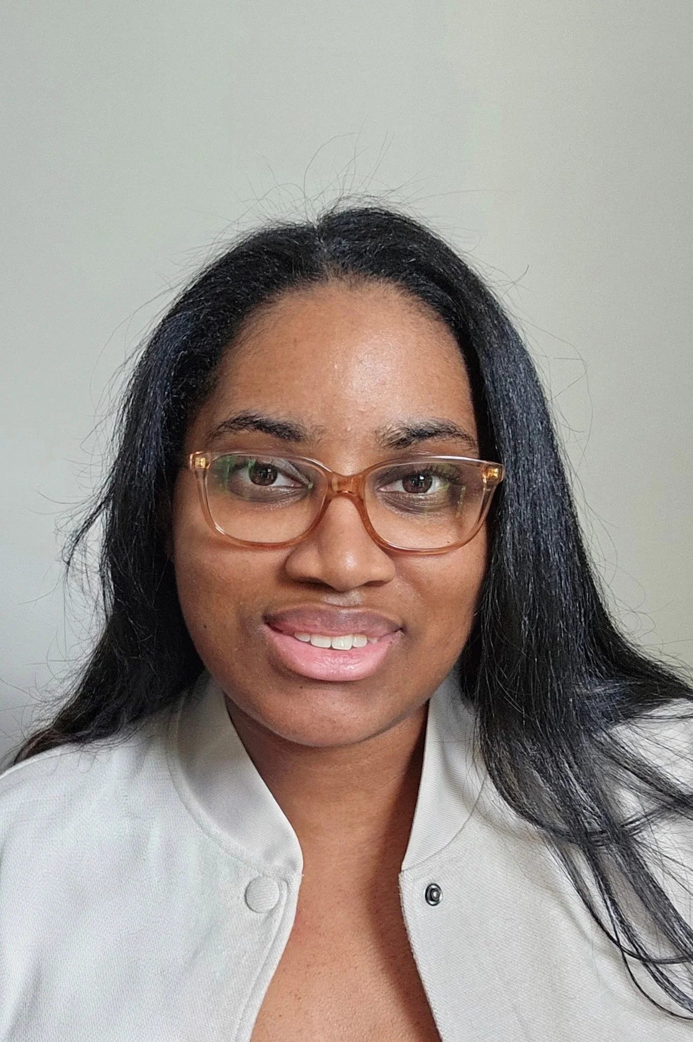 Close-up photo of a woman wearing glasses, with dark hair and a white collared shirt, smiling against a plain background.