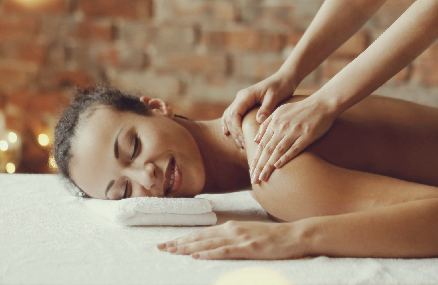 Woman receiving a back massage in a spa or massage room with a brick wall background.