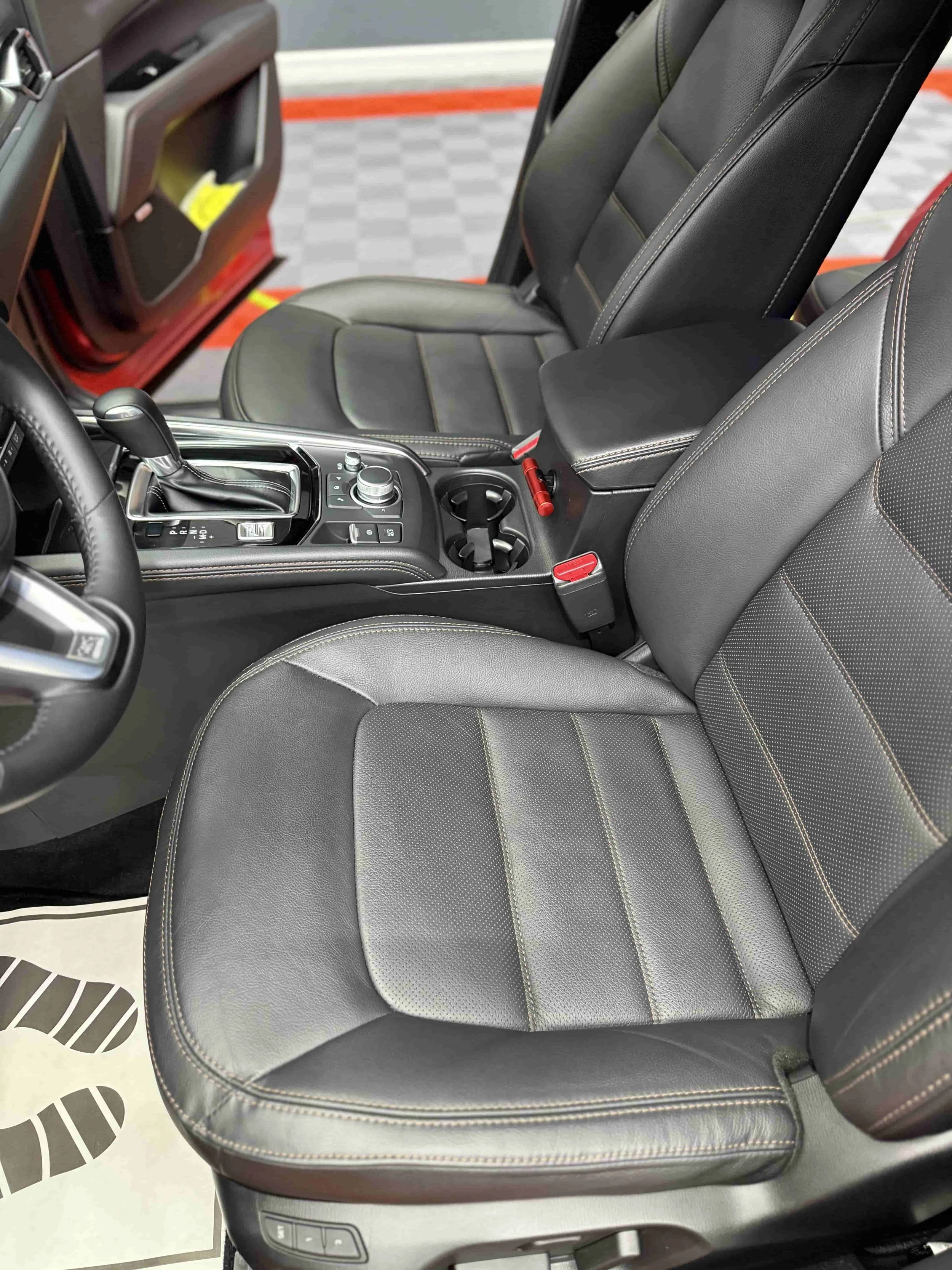 Der Innenraum eines Autos mit schwarzen Ledersitzen, Schalthebel, Steuerungsknöpfen und Cupholder im Mittelfeld.