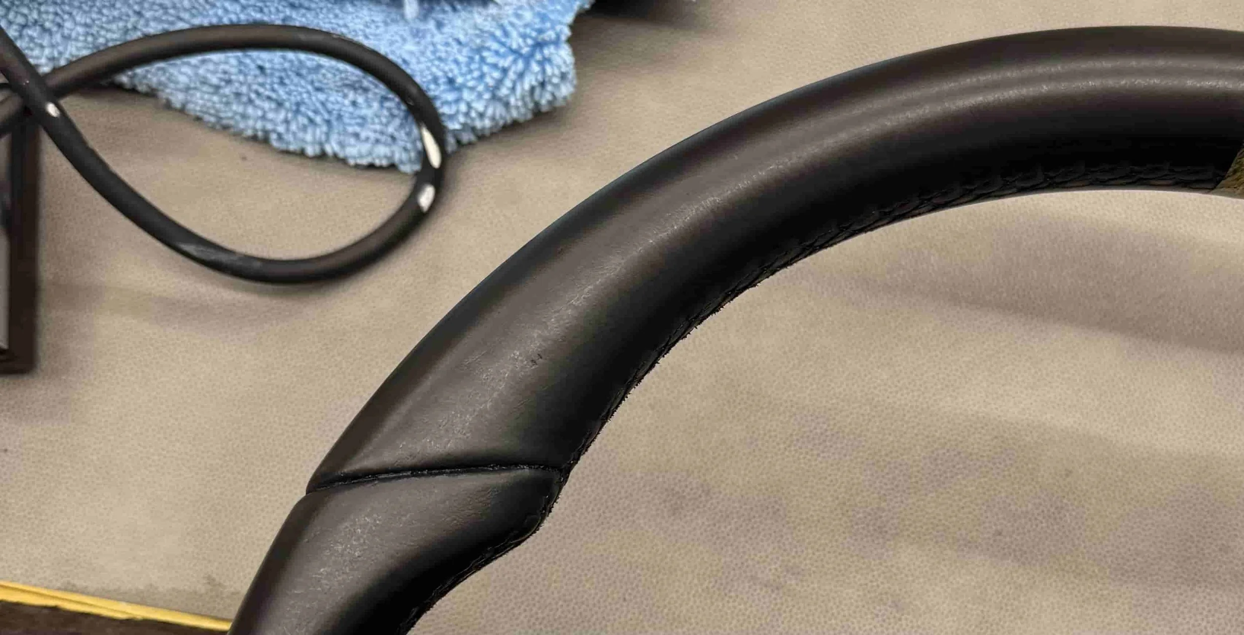 Nahaufnahme eines schwarzen Fahrradlenkers auf einem beige-farbenen Untergrund. Im Hintergrund liegt eine blaue Reinigungsschwamm und eine schwarze Kabelrolle.