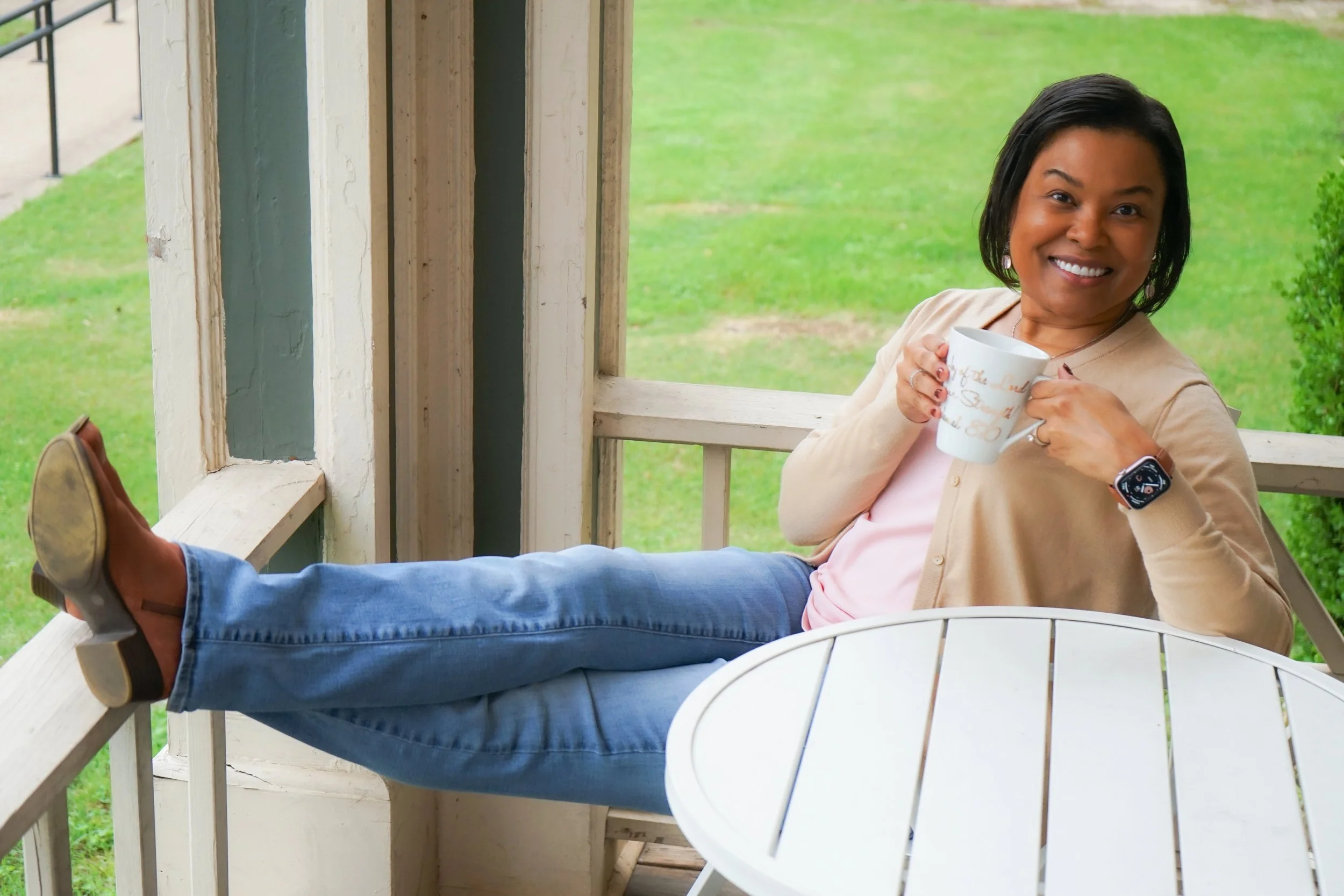 woman sitting in chair, holding white coffee mug, with feet on railing