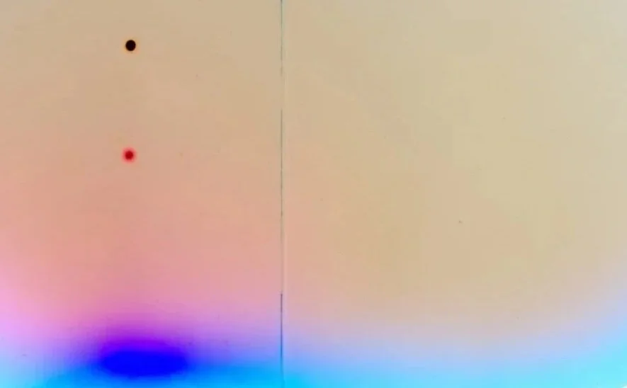 Close-up of a light-colored wall with two small colored dots, one black and one red, and a faint vertical line dividing the image, with a gradient rainbow effect near the bottom.