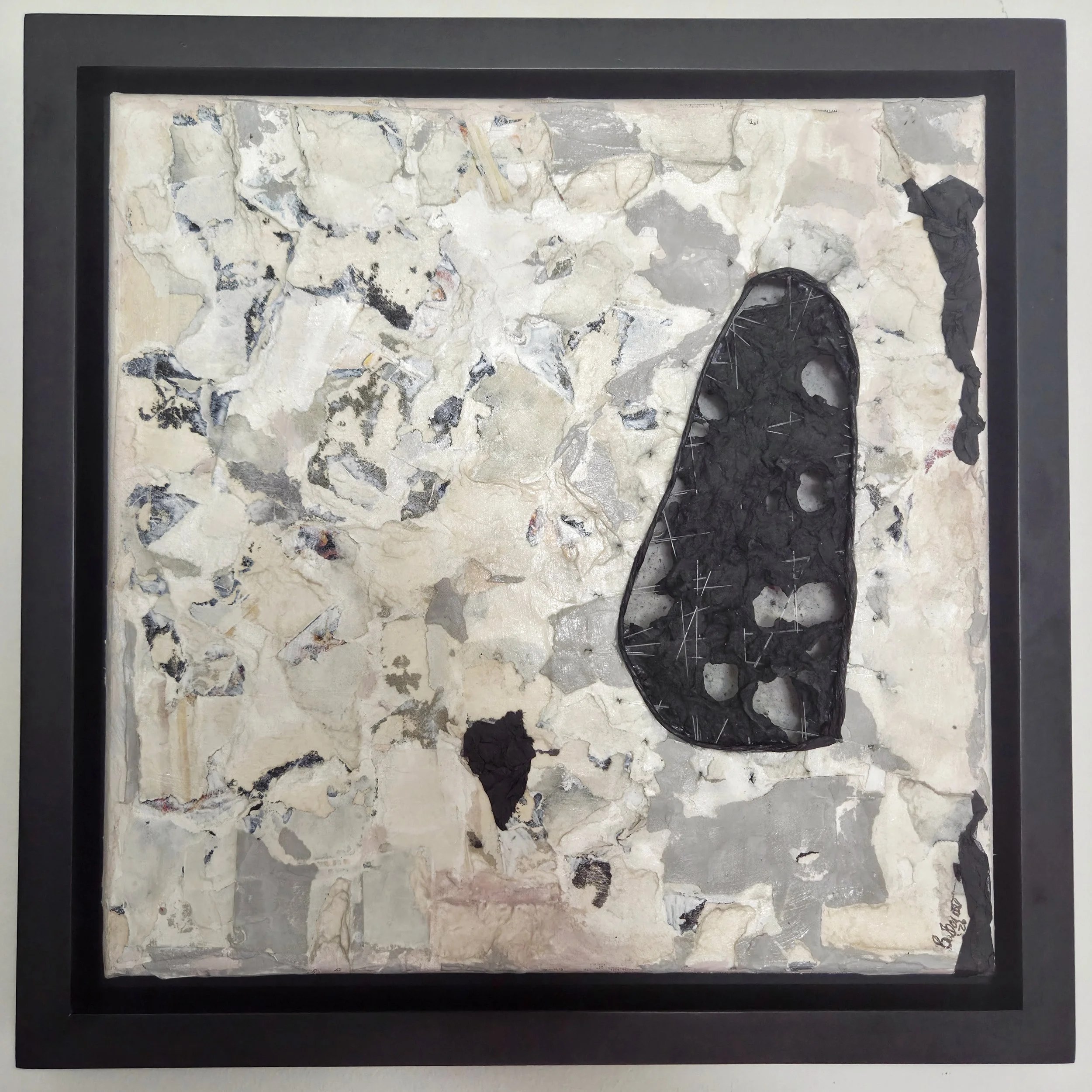 Close-up view of a framed abstract artwork with a textured surface made of various stone fragments in shades of cream, gray, and black, with some dark patches and irregular patterns.