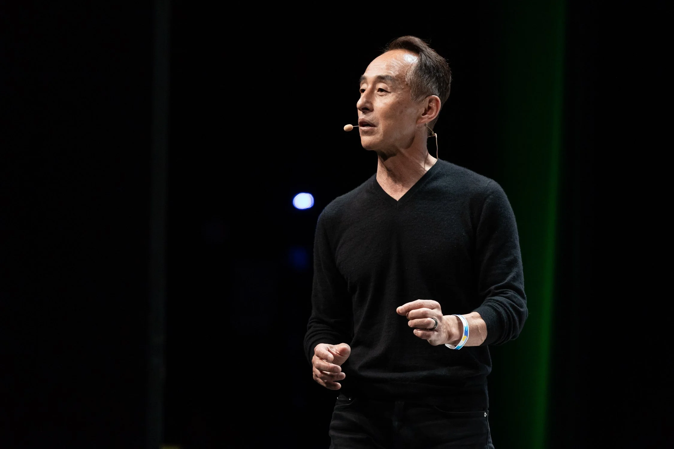 A man in a black sweater giving a presentation on stage with a microphone headset.