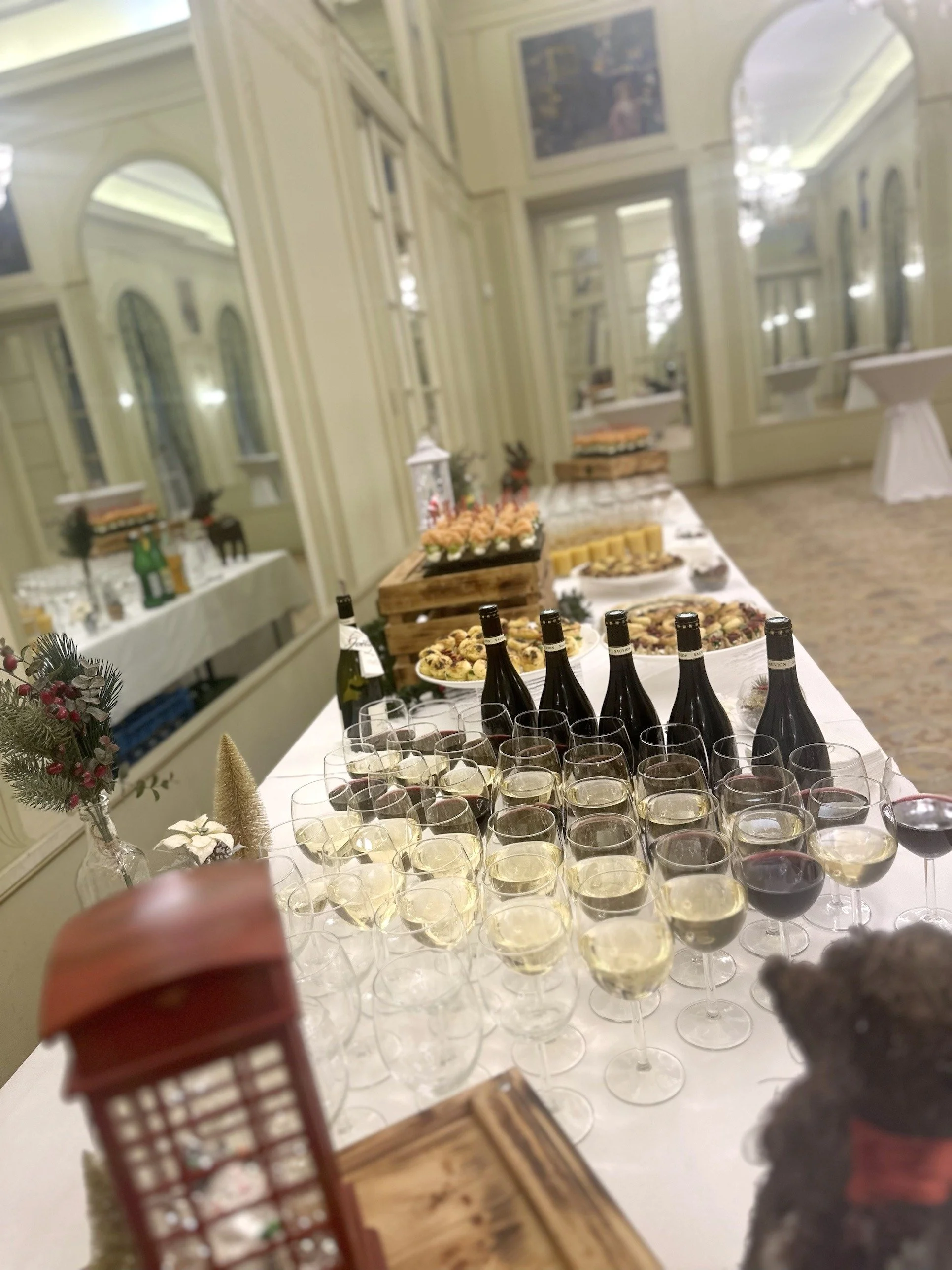 A table set for a celebration with glasses of white and red wine, snacks, and decorations in a bright room with large windows and mirrors.