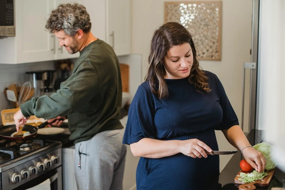 A man and woman in kitchen, man cooking at stove, woman chopping lettuce and tomato representing htose who work with naturopath Eloise smith