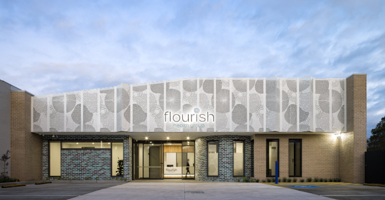 Exterior view of a modern building with a white decorative facade, glass entrance doors, and a sign that reads 'flourish heart center'.