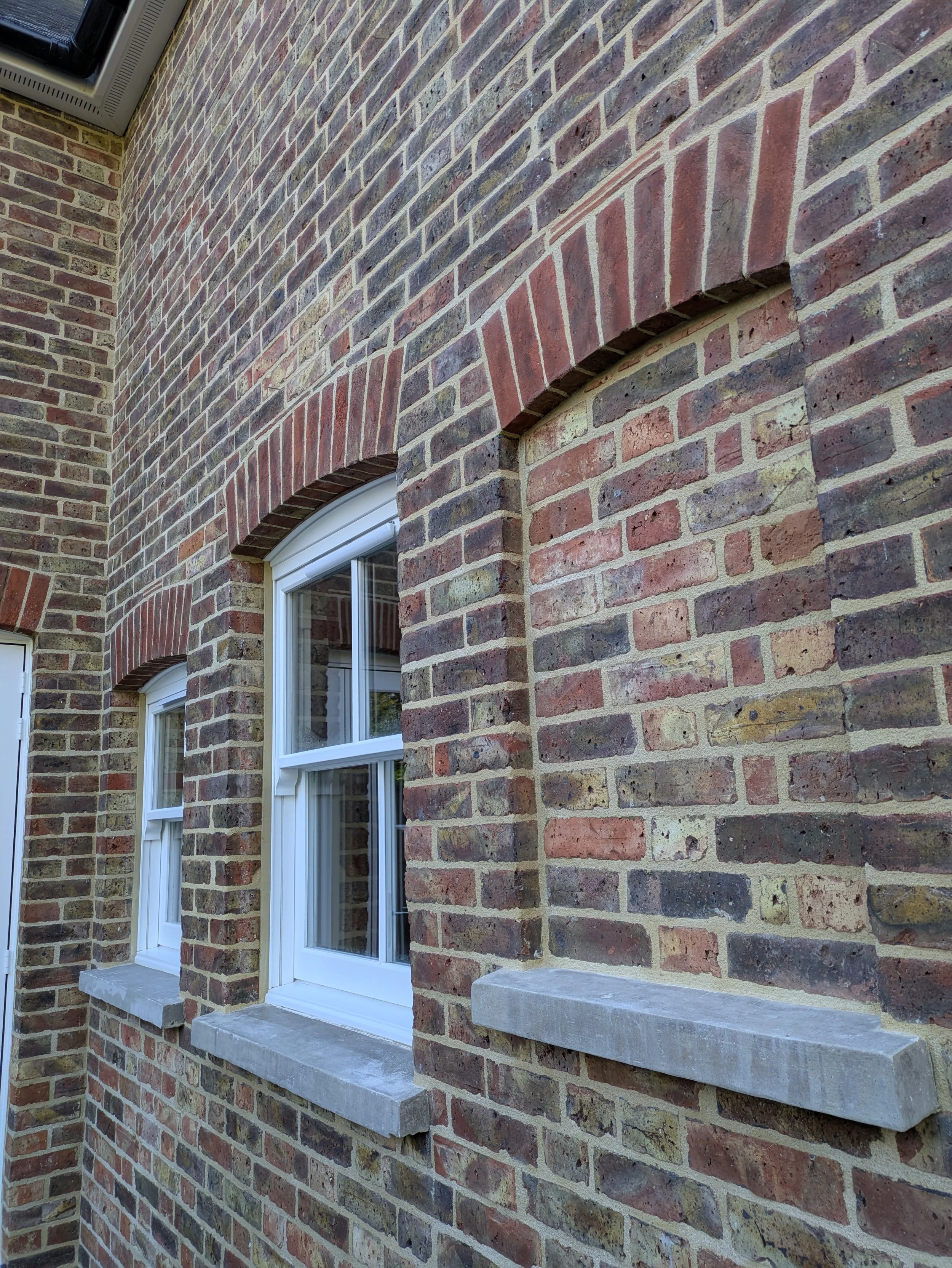 Exterior brick wall of a period house with red brick arches above the windows, pointed with traditional lime mortar.