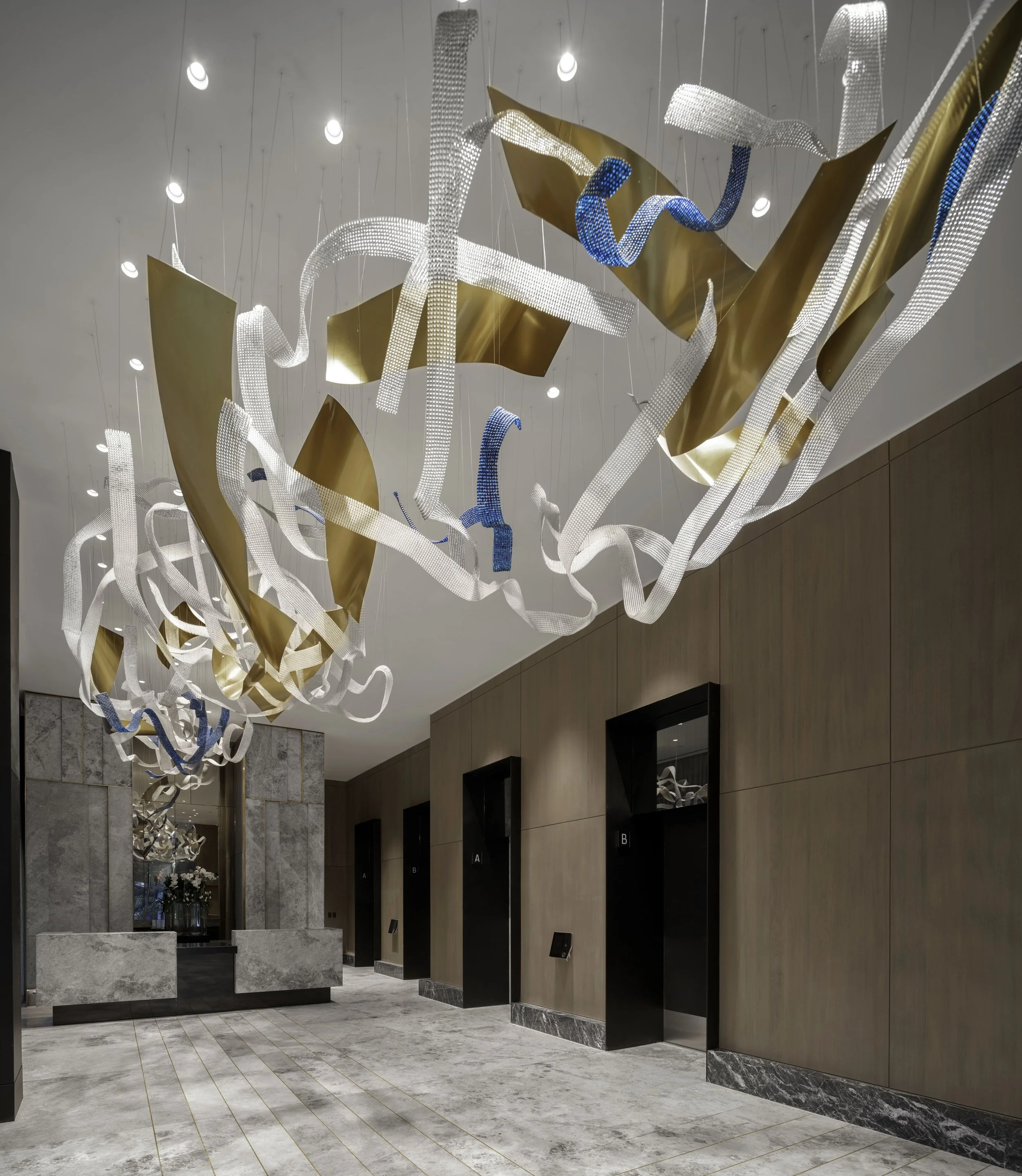 Modern hotel lobby with abstract chandelier featuring gold, white, and blue ribbon-like elements hanging from the ceiling.