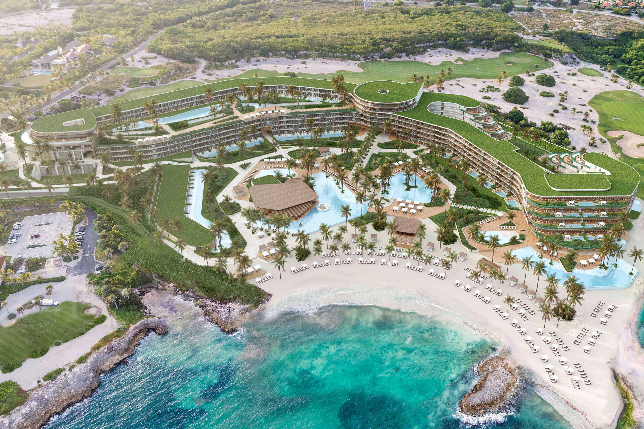 Aerial view of a luxurious beachfront resort with multiple swimming pools, a sandy beach with lounge chairs, palm trees, and a modern, curved building with green rooftops, situated next to the ocean.