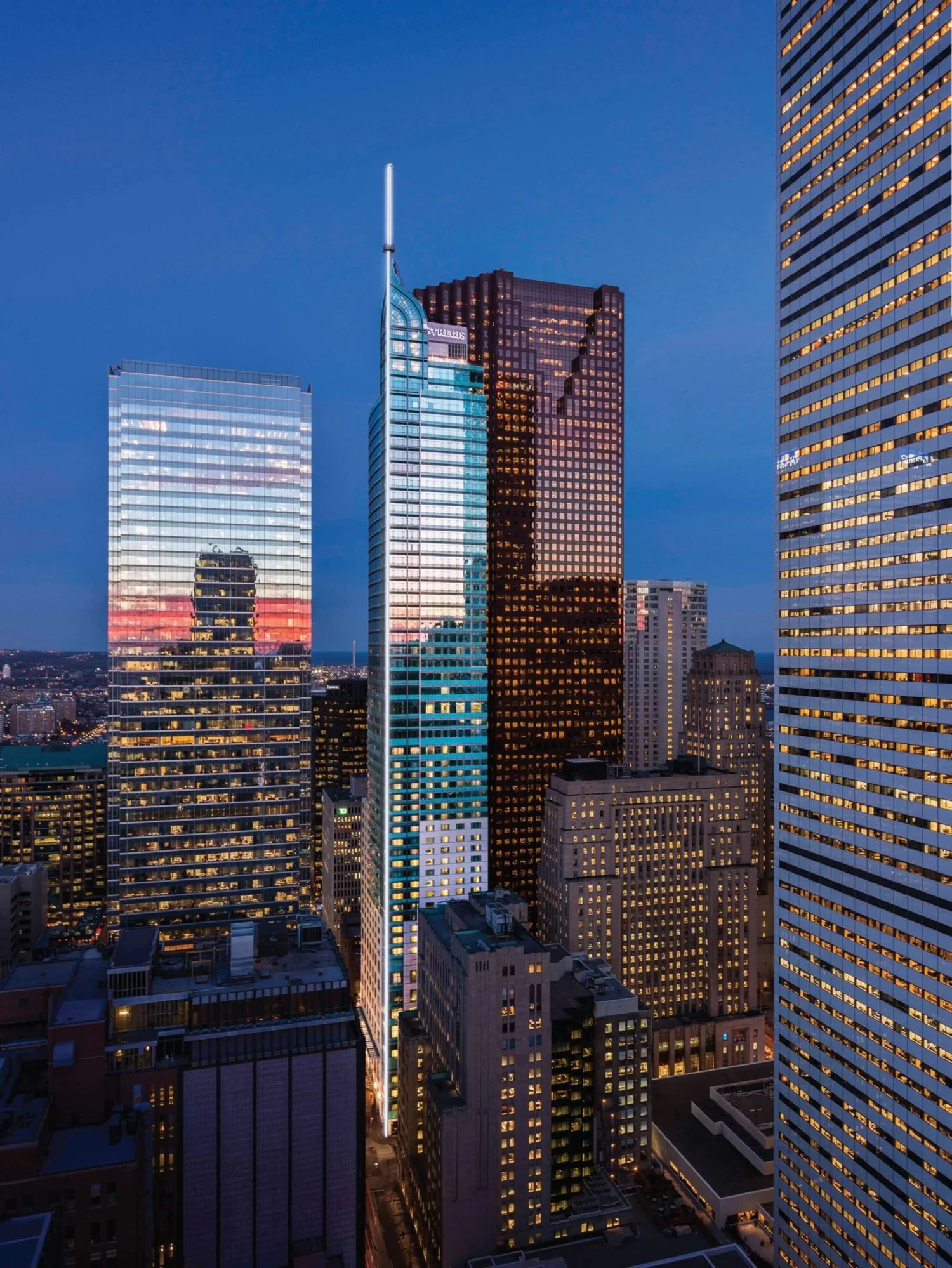 City skyline at dusk featuring tall glass skyscrapers with illuminated windows, reflecting the twilight sky.