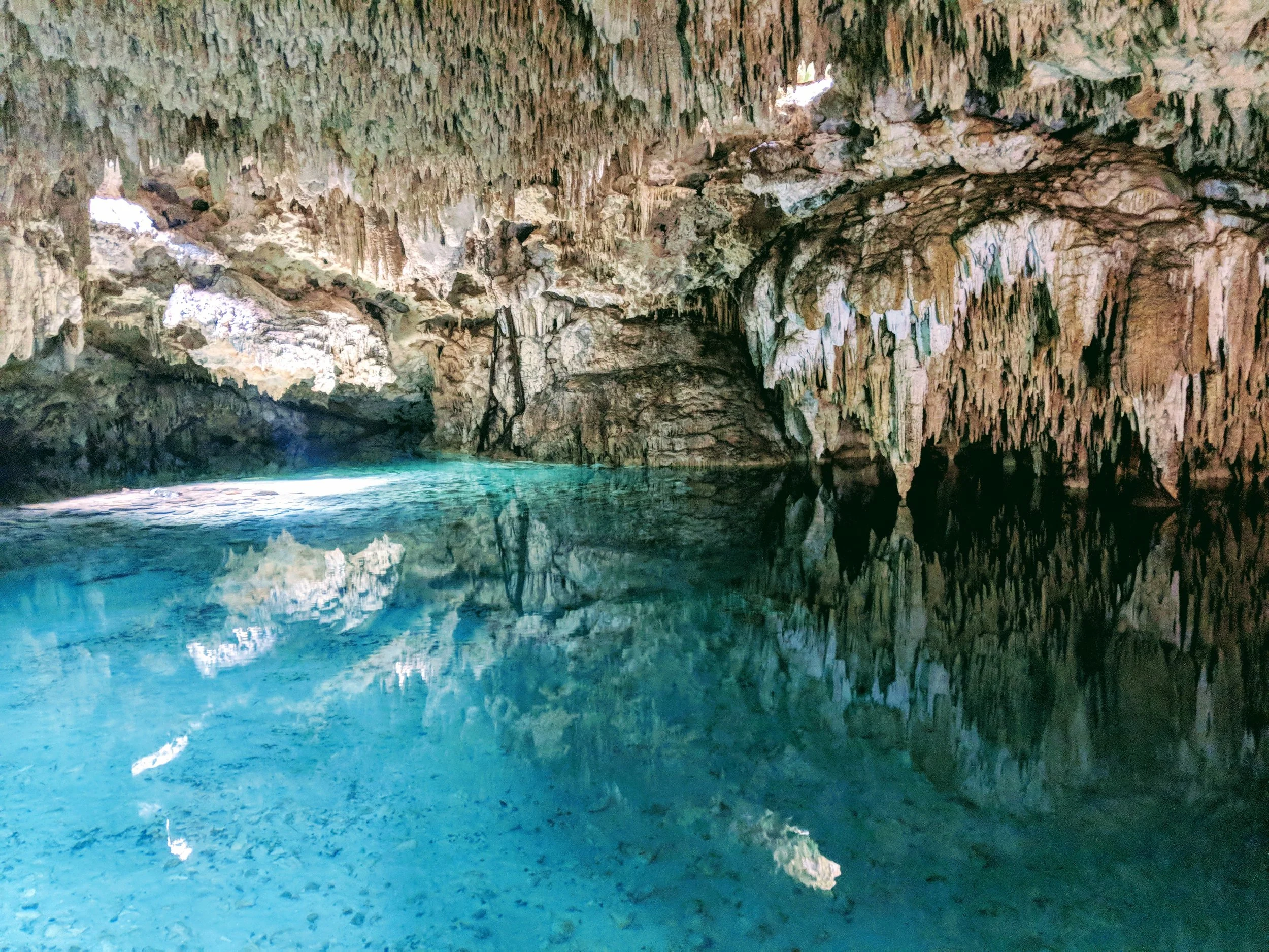 Inside a cave with clear blue water and stalactites hanging from the ceiling.