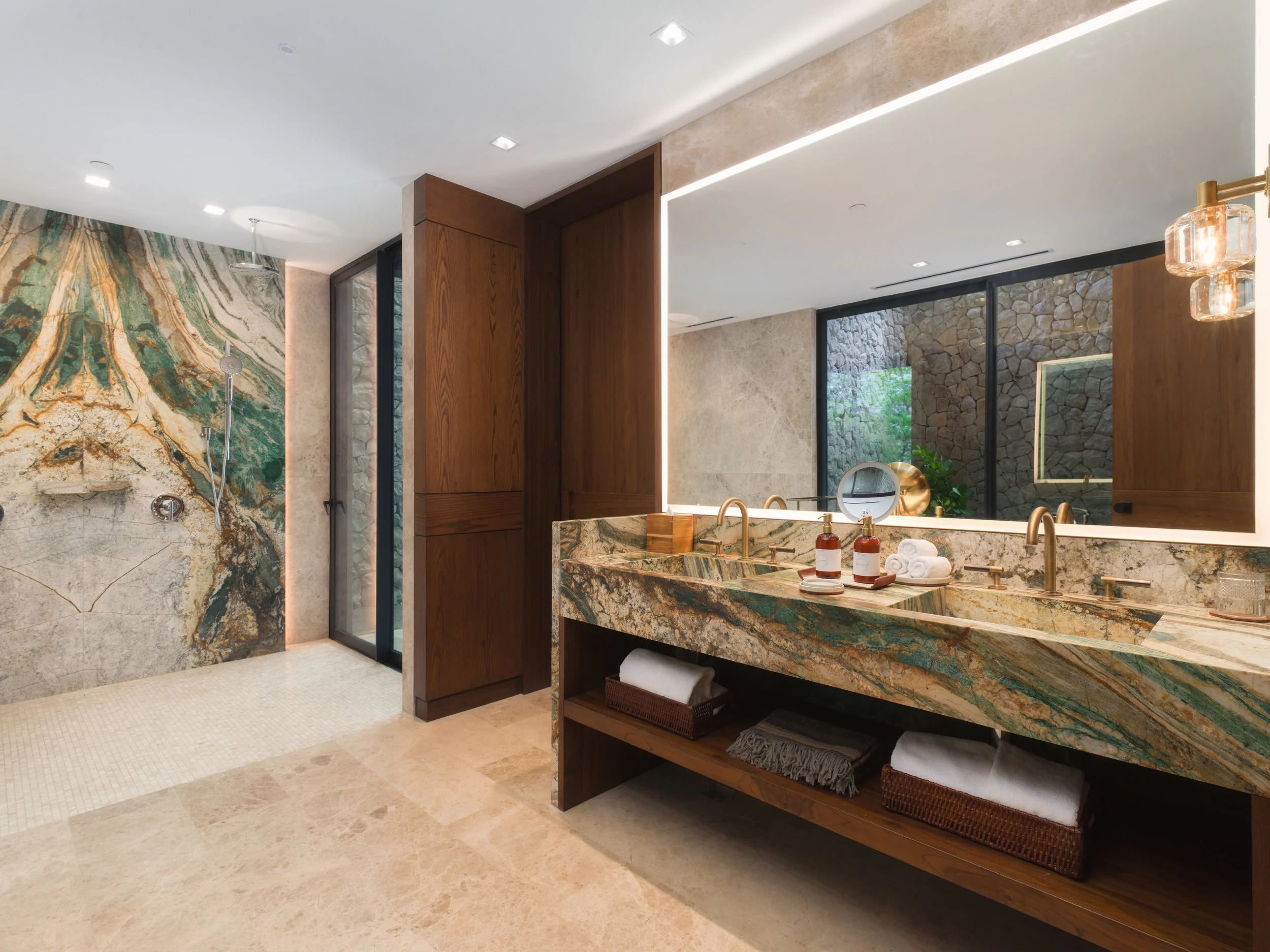 Luxurious bathroom with a double marble sink, large mirror, wooden cabinetry, stone accents, and a walk-in shower with marble walls.