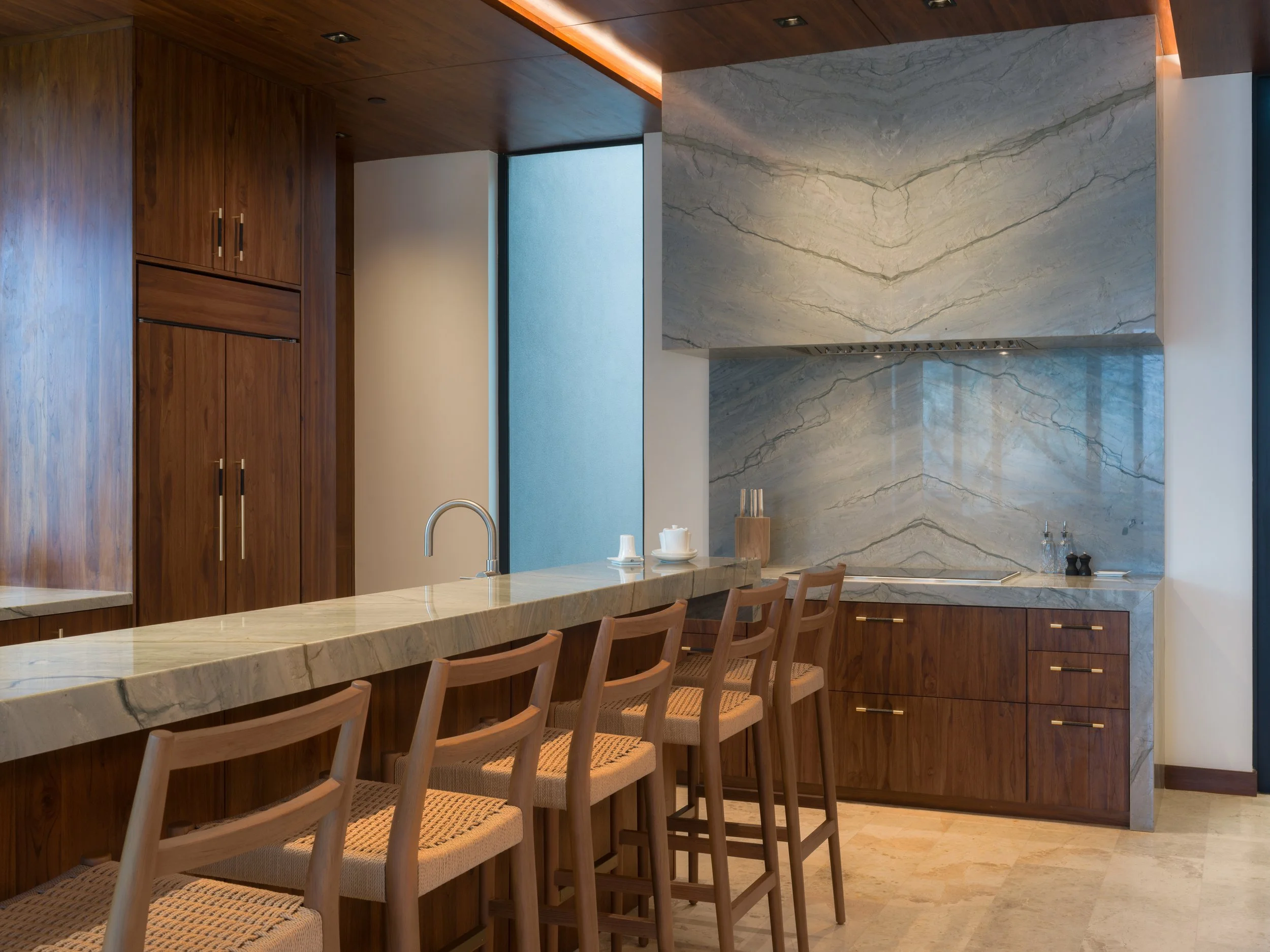 Modern kitchen with wooden cabinets, marble countertops, and a breakfast bar with four chairs.